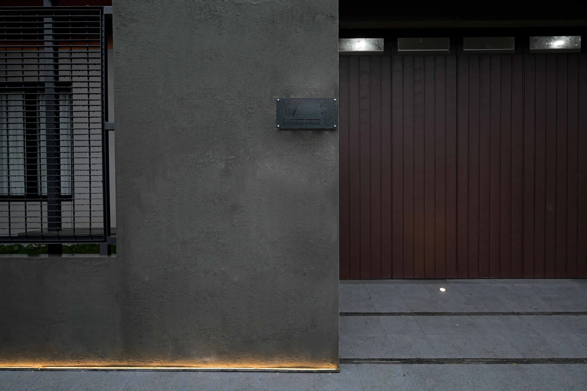 House number plaque set into the concrete pillar beside the timber front door, its slatted surface lit by a recessed floor light.