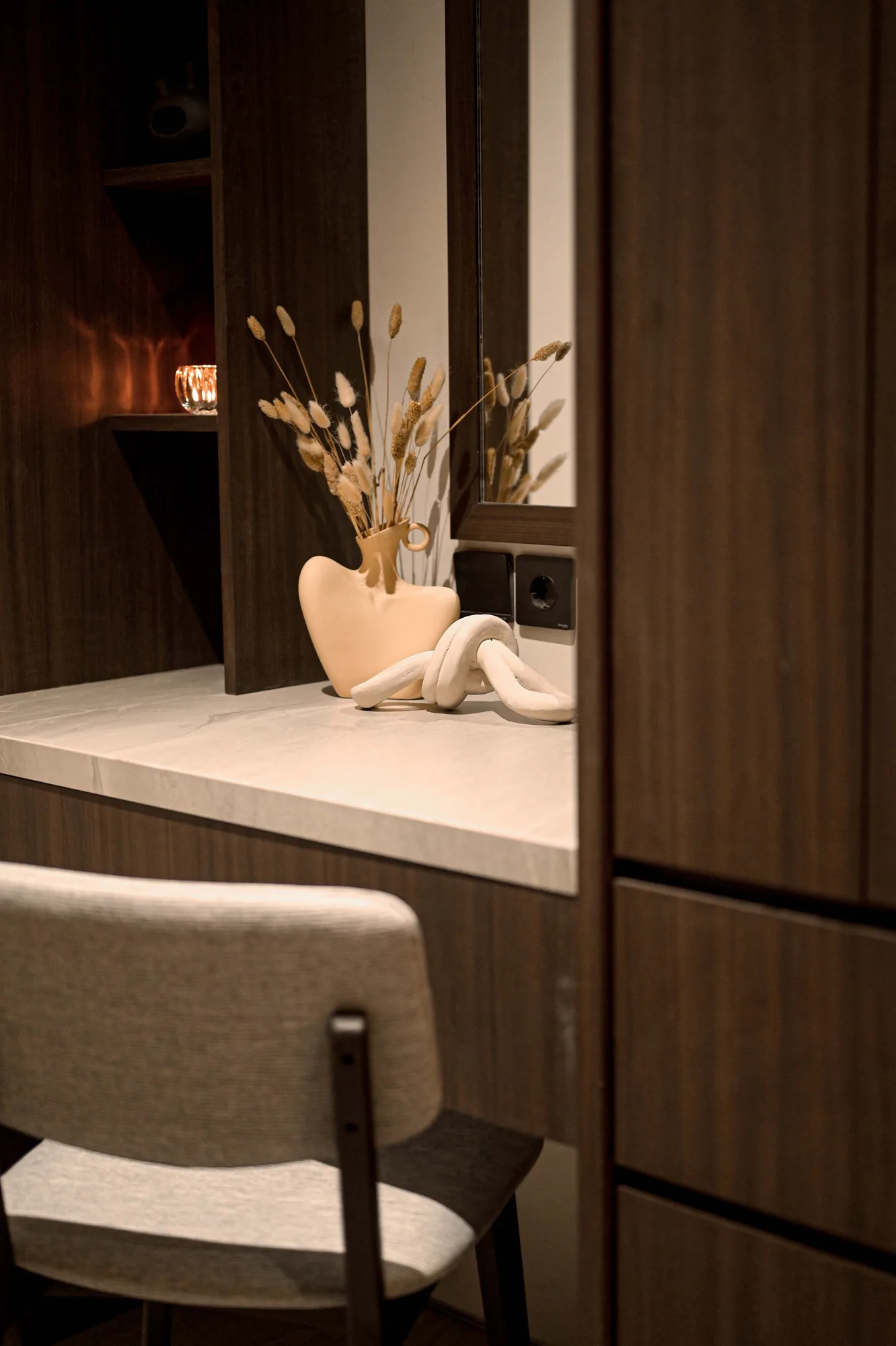 Dressing counter detail, a knotted ceramic sculpture beside a vase of dried pampas grass reflected in the mirror.