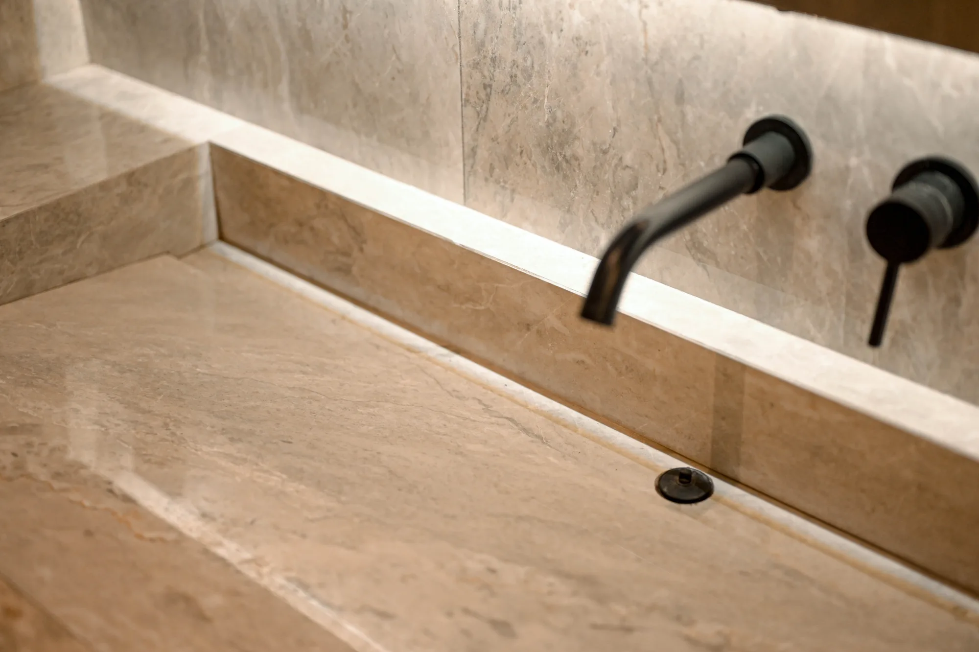 Close-up of the trough sink's stone basin and matte black wall-mounted taps.