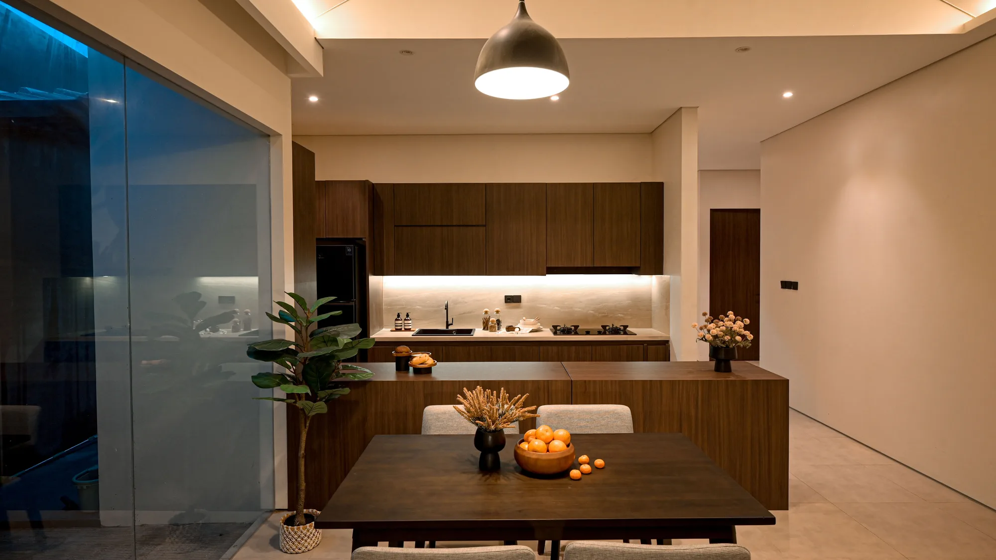 Open kitchen and dining area with a dark walnut island, a black pendant lamp over the dining table, and a sliding glass door to the courtyard.