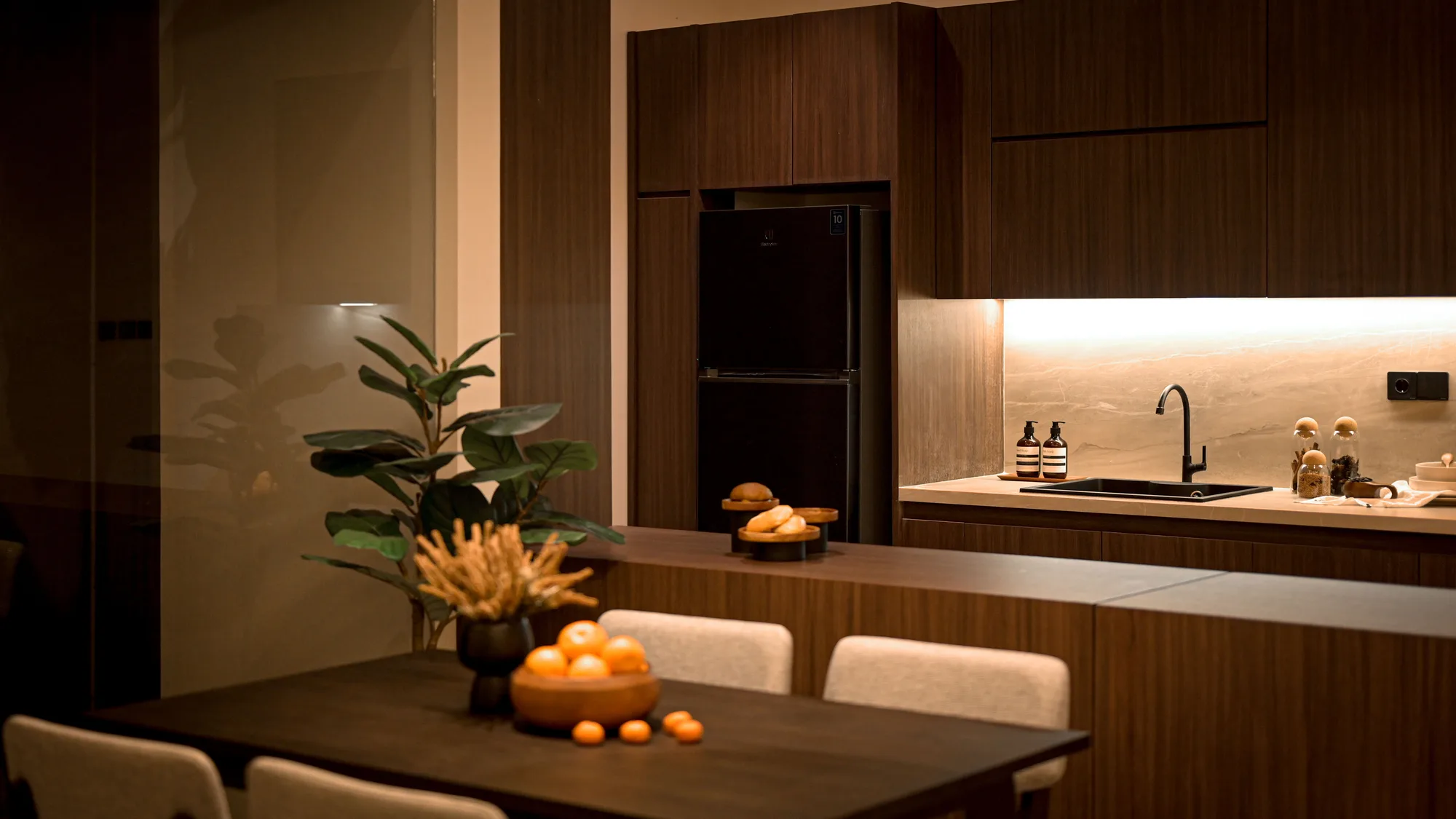 Kitchen sink and stone backsplash beside the built-in fridge, with the dining table and its bowl of citrus in the foreground.