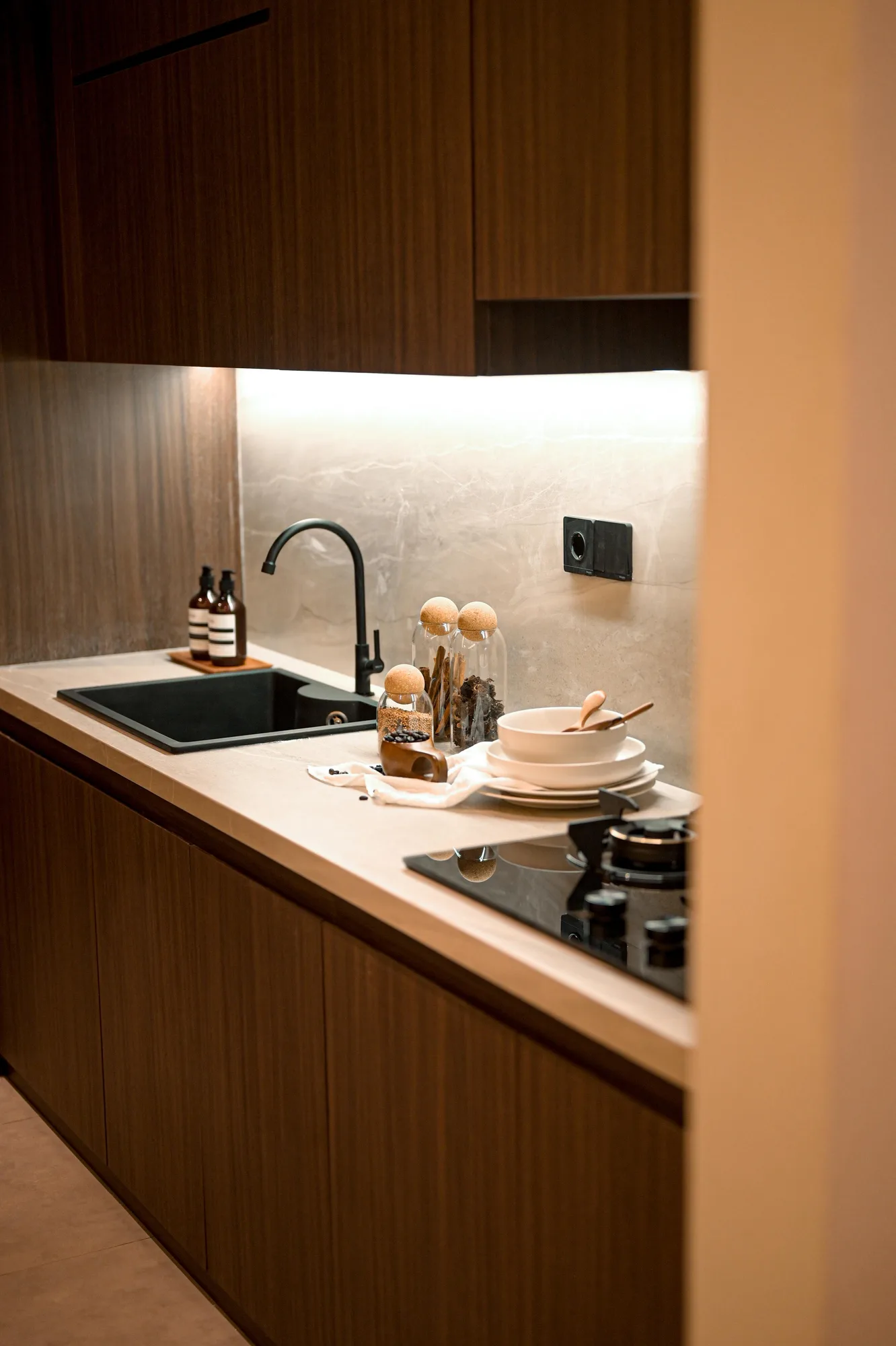 Kitchen counter detail with black tap, jarred spices and stacked bowls against a stone backsplash.
