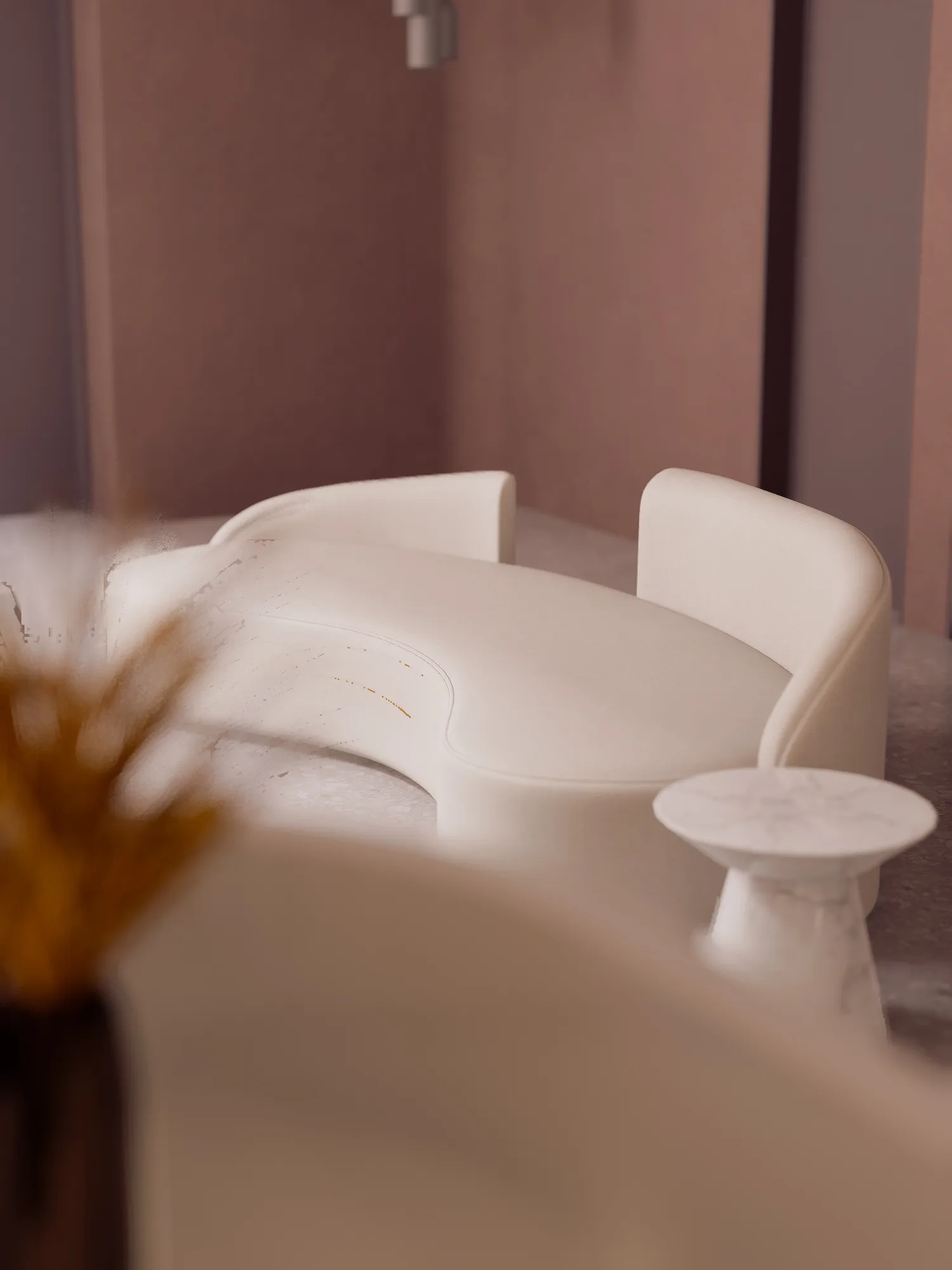 A curved cream bench and marble-look side table inside Beauty Center, seen past a dried grass arrangement in the foreground.