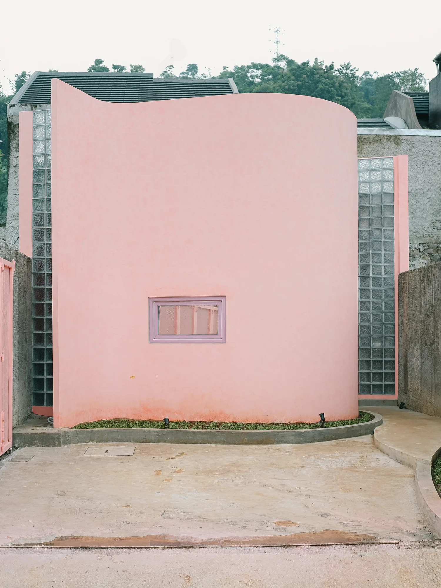 Bersemi di Kediaman's curved pink facade rising above its perimeter wall, a glass block strip marking the edge beside it.