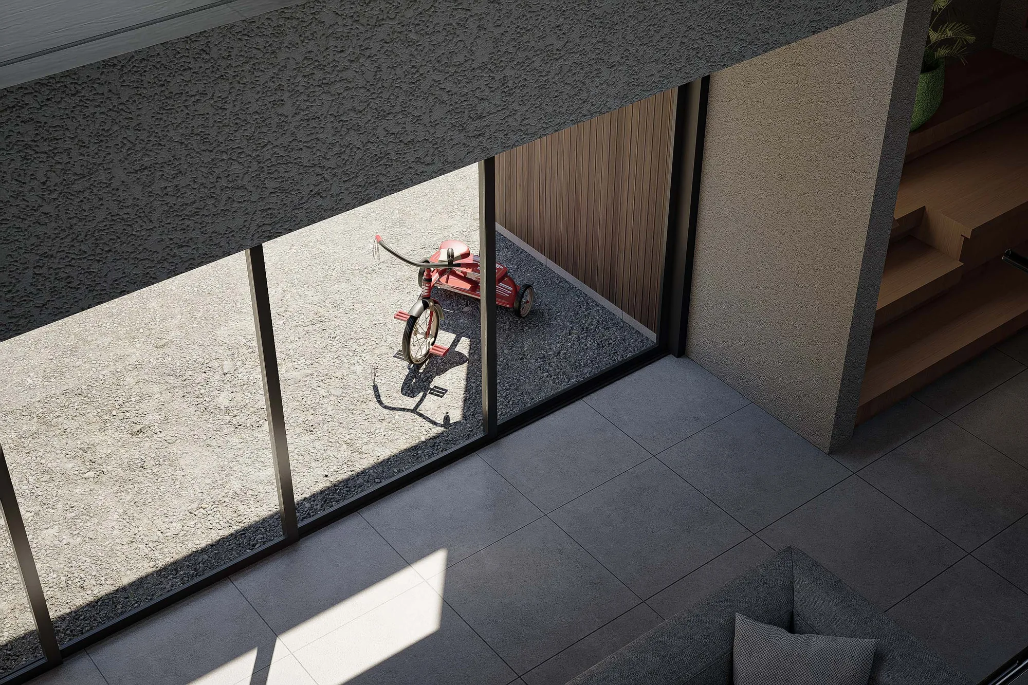 Overhead view of a red tricycle left on the gravel courtyard, seen through the open sliding door of the living room.