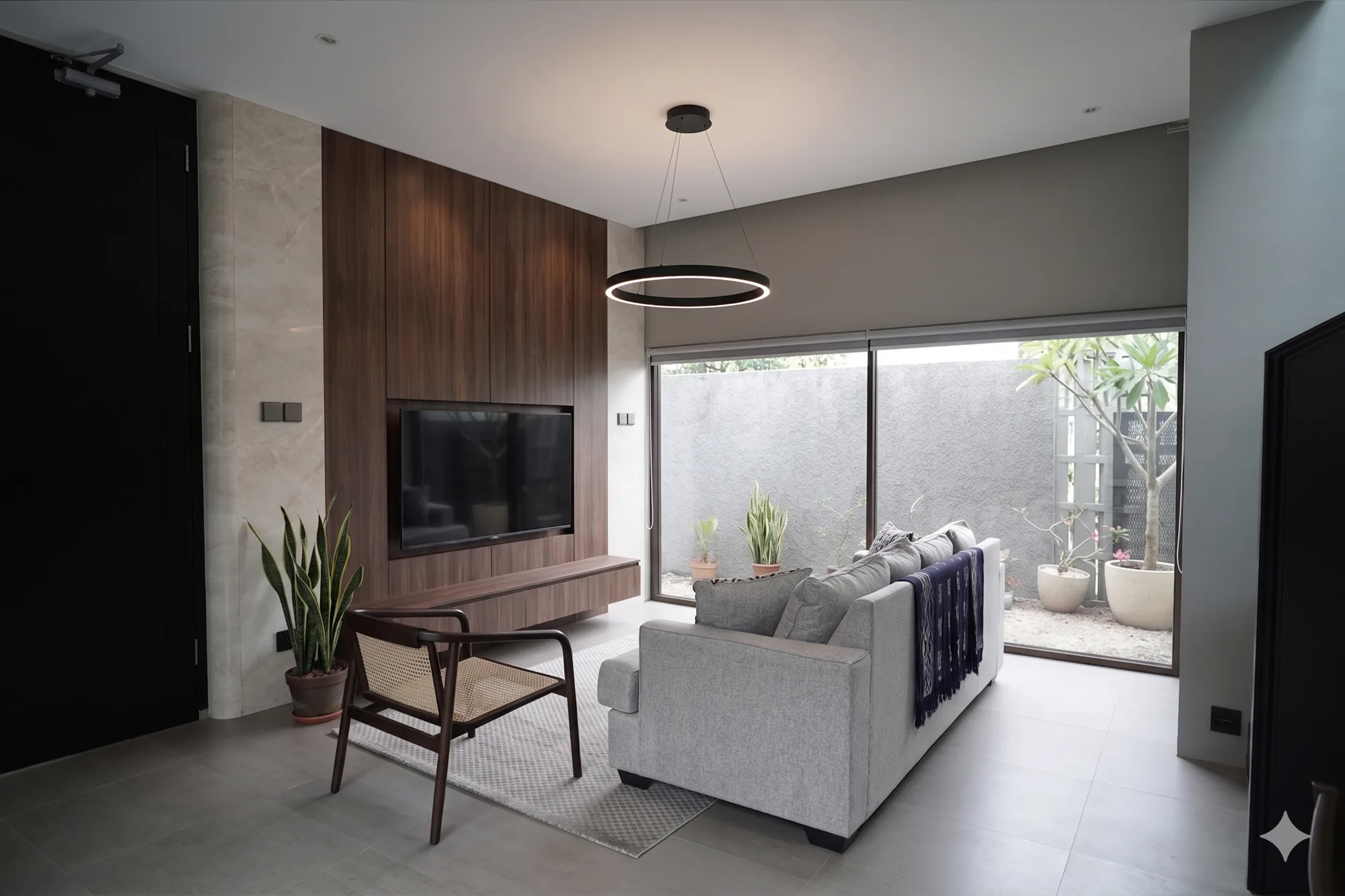 The living area's walnut-paneled media wall faces a grey sofa and cane-seated chair, sightlines running past to a glazed sliding door onto the enclosed side yard.