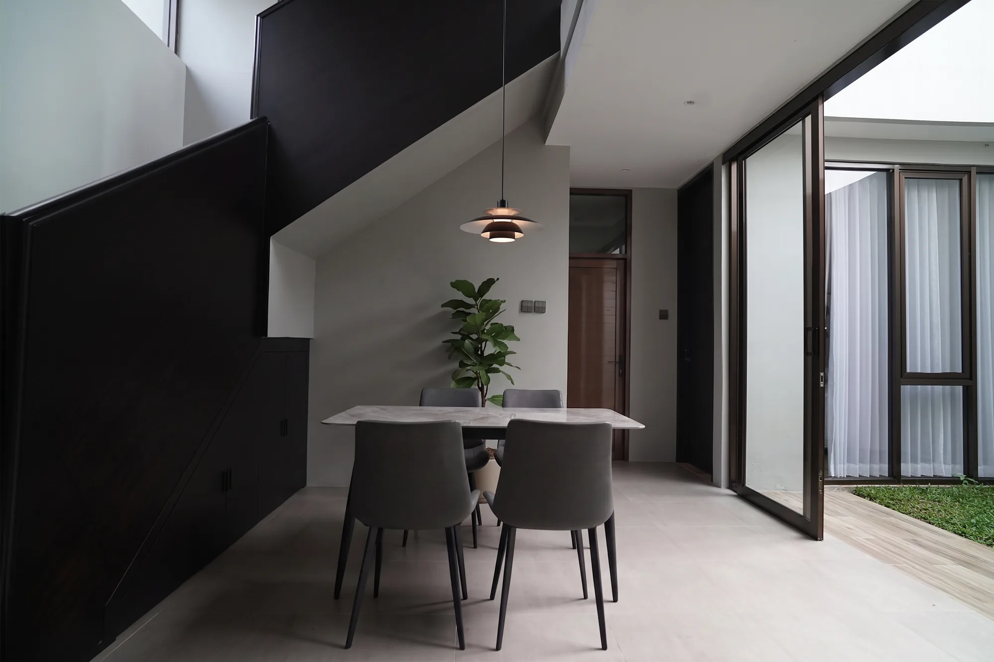 Beneath the open stair, a marble dining table and pendant lamp sit open to the wood front door on one side and a glazed sliding door onto the courtyard on the other.