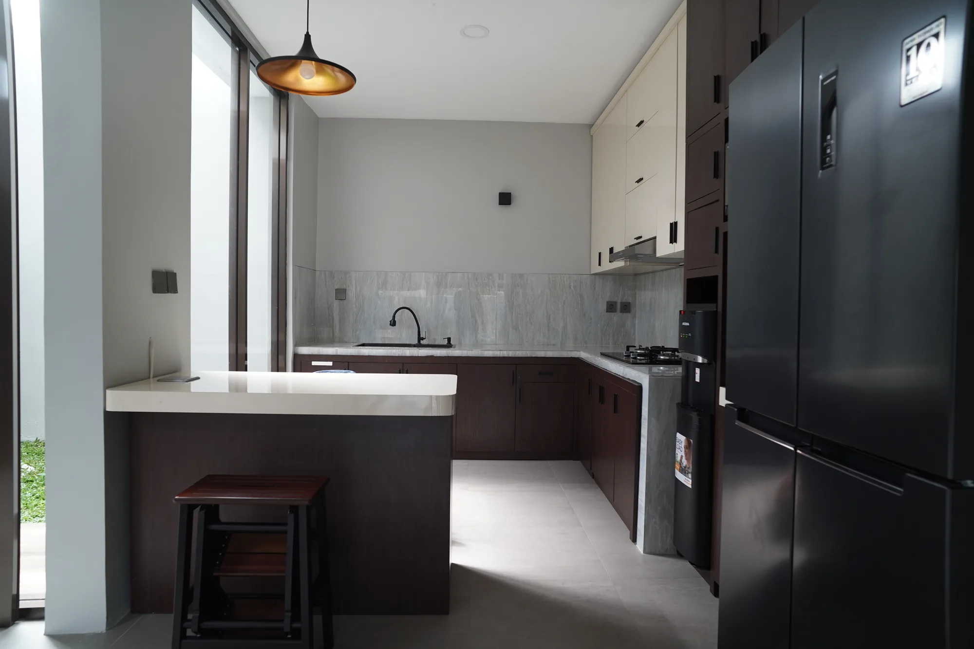 The kitchen's dark wood lower cabinets meet cream upper units along a grey marble backsplash, a white peninsula counter extending toward the glazed side entrance.