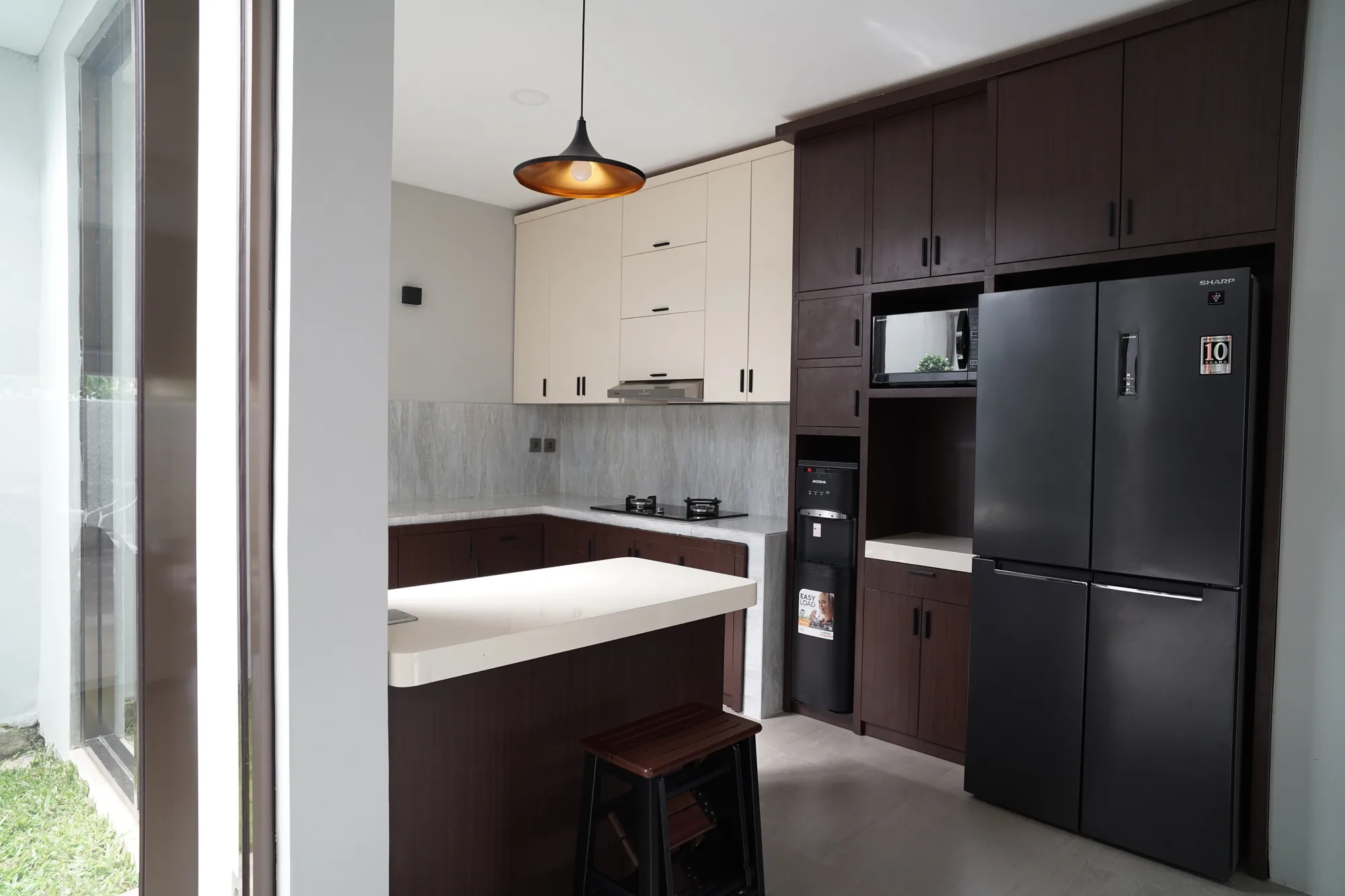Floor-to-ceiling dark wood cabinetry frames a black refrigerator and built-in microwave, cream upper units continuing above a white-topped island counter.