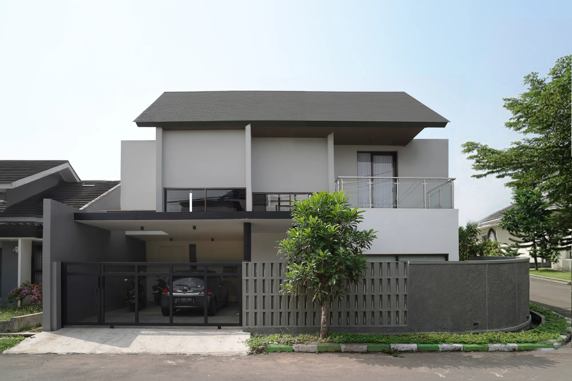 Hook House's corner-lot face by day: a dark tiled roof lifted clear above pushed-and-pulled white volumes, a glazed balcony rail, and a mesh gate sheltering the car beneath the carport.
