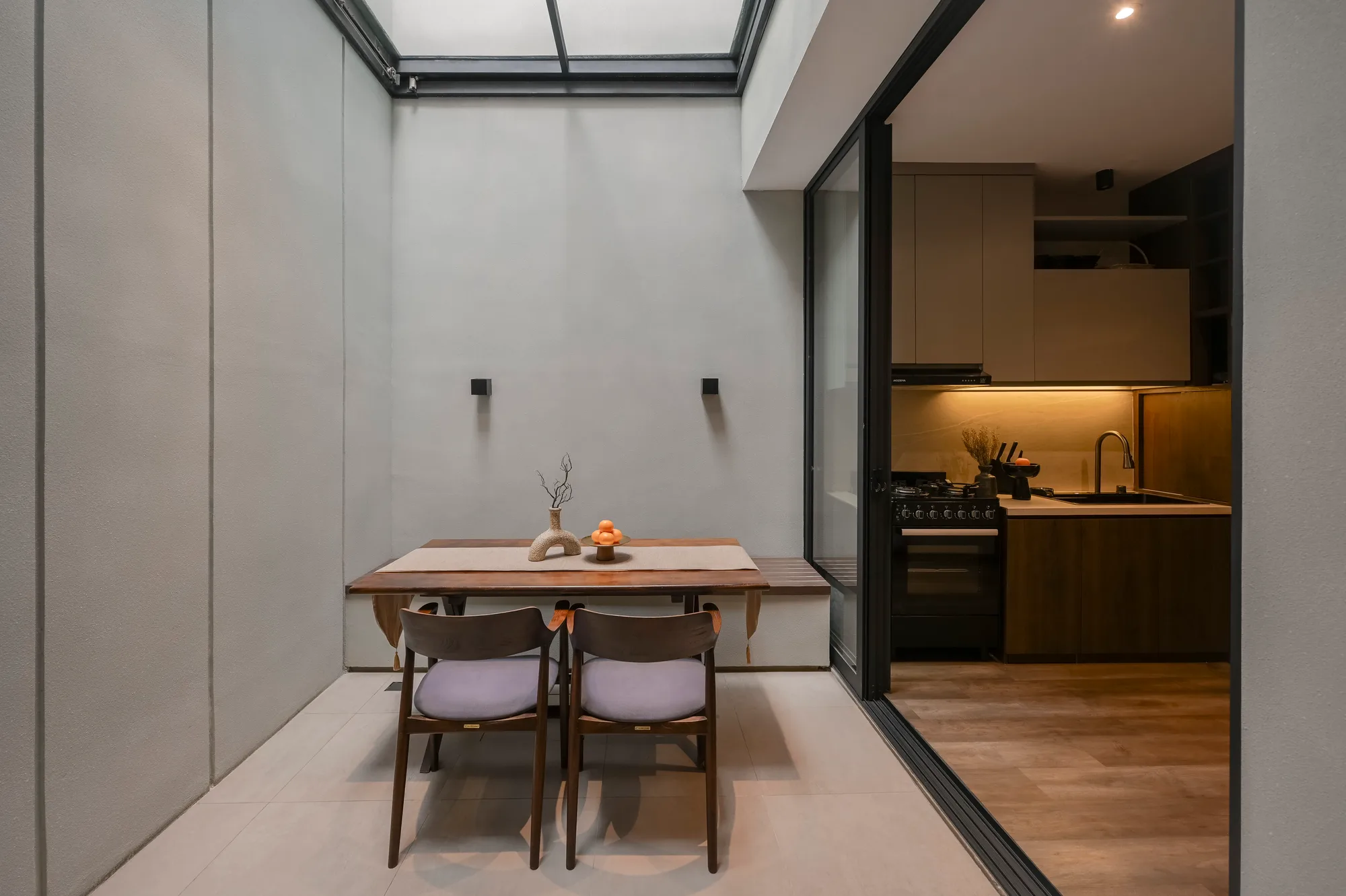 Dining table centered beneath the open retractable roof, daylight falling on the concrete-look walls.