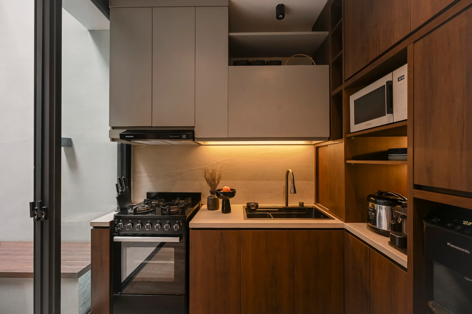 Kitchen counter with a gas range and sink beneath under-cabinet lighting, the courtyard door open beside it.