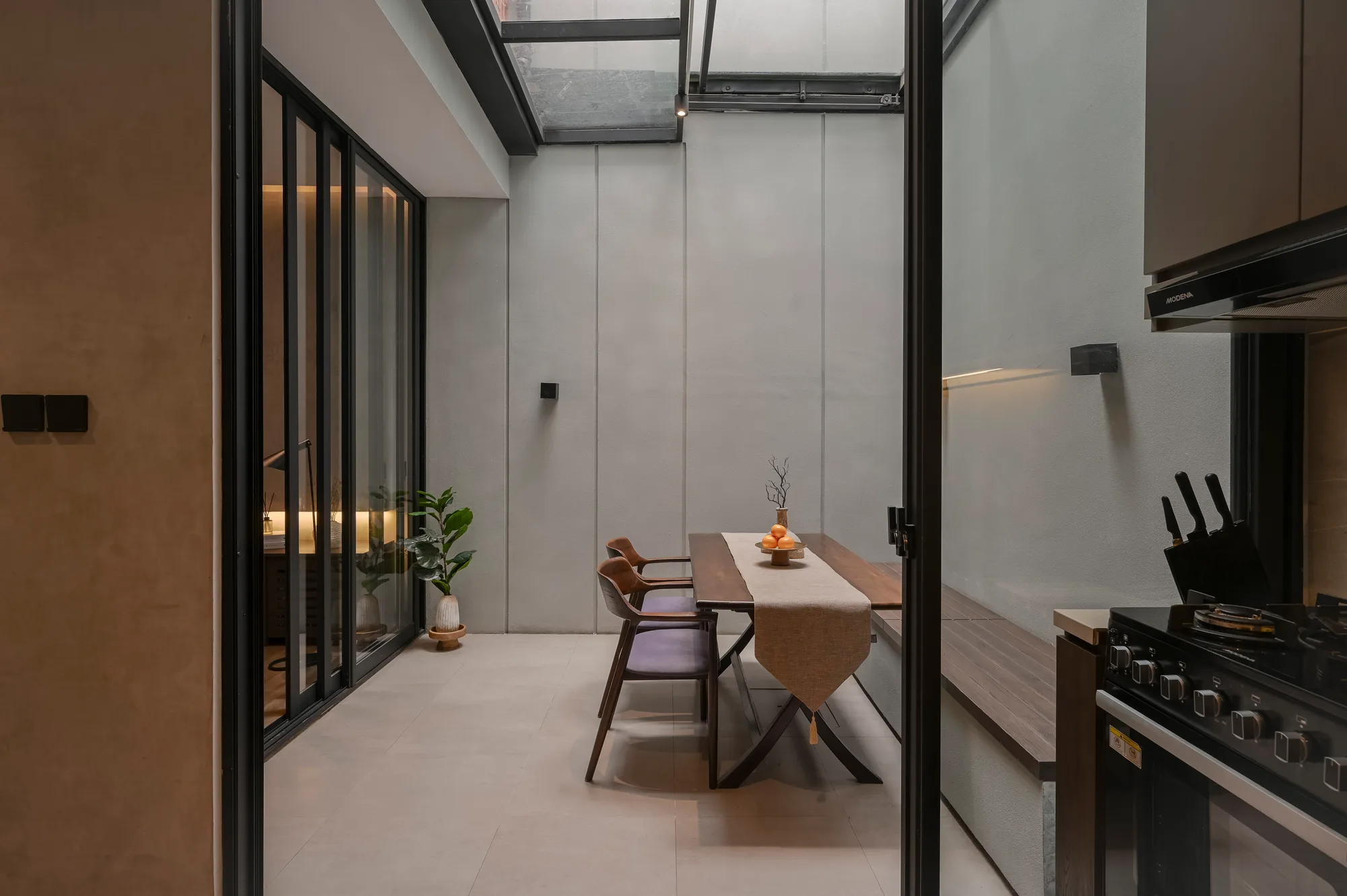 Dining area under the retractable roof, seen from the living room with the kitchen opening beyond.