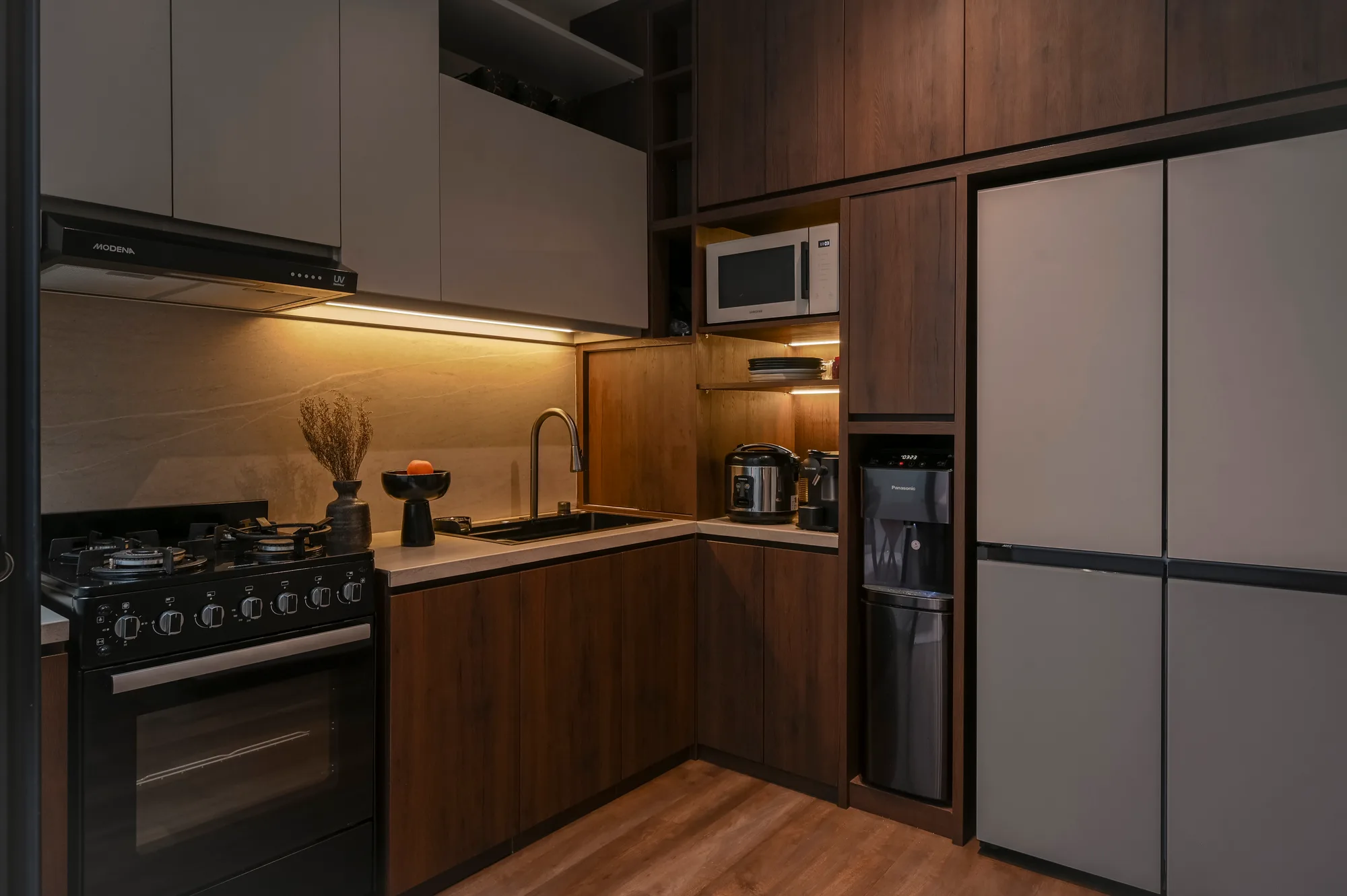 Kitchen corner with the refrigerator, microwave and rice cooker nook against wood-panelled cabinetry.