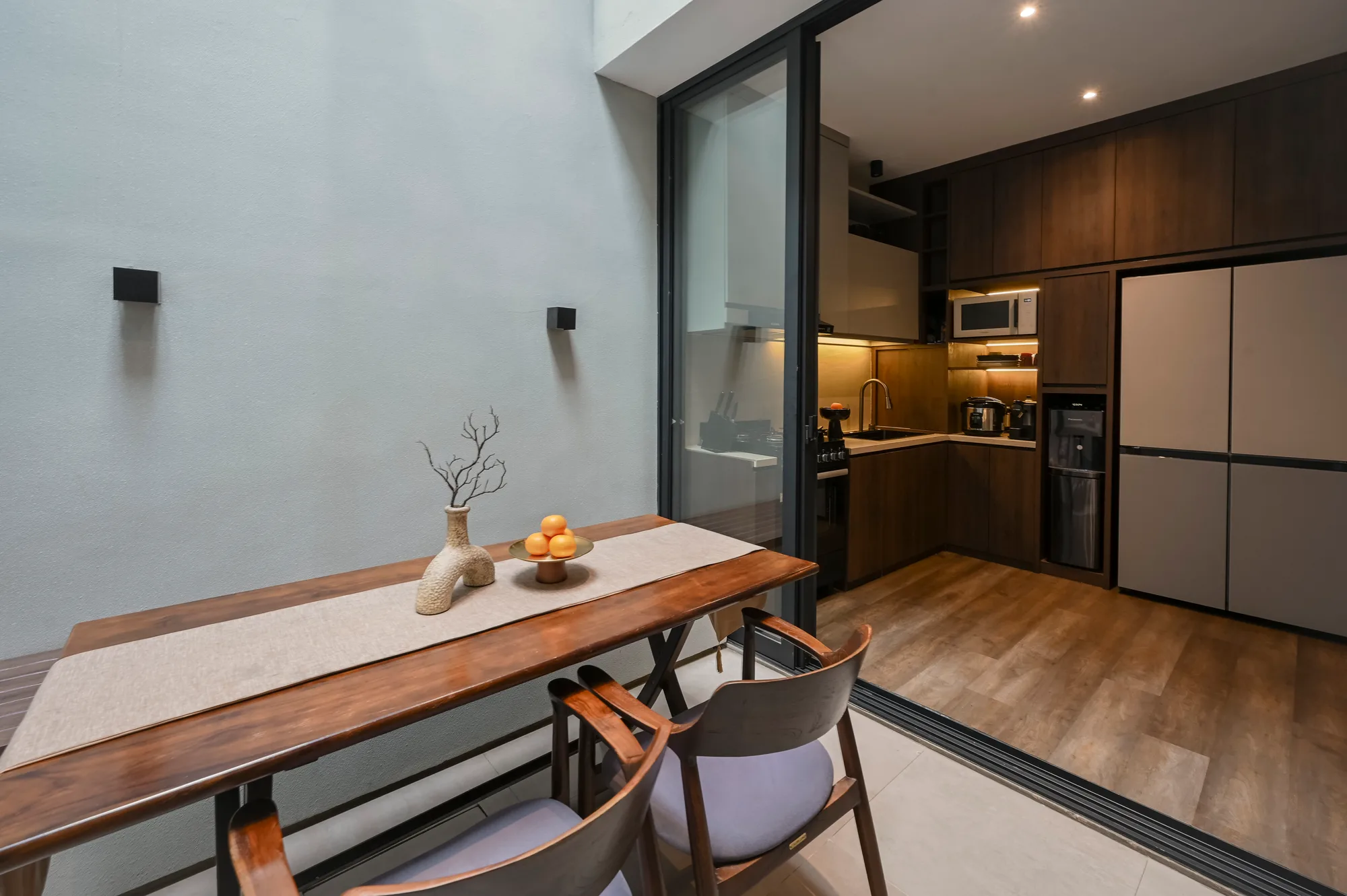 Dining area and kitchen seen together, the refrigerator visible past the open sliding door.
