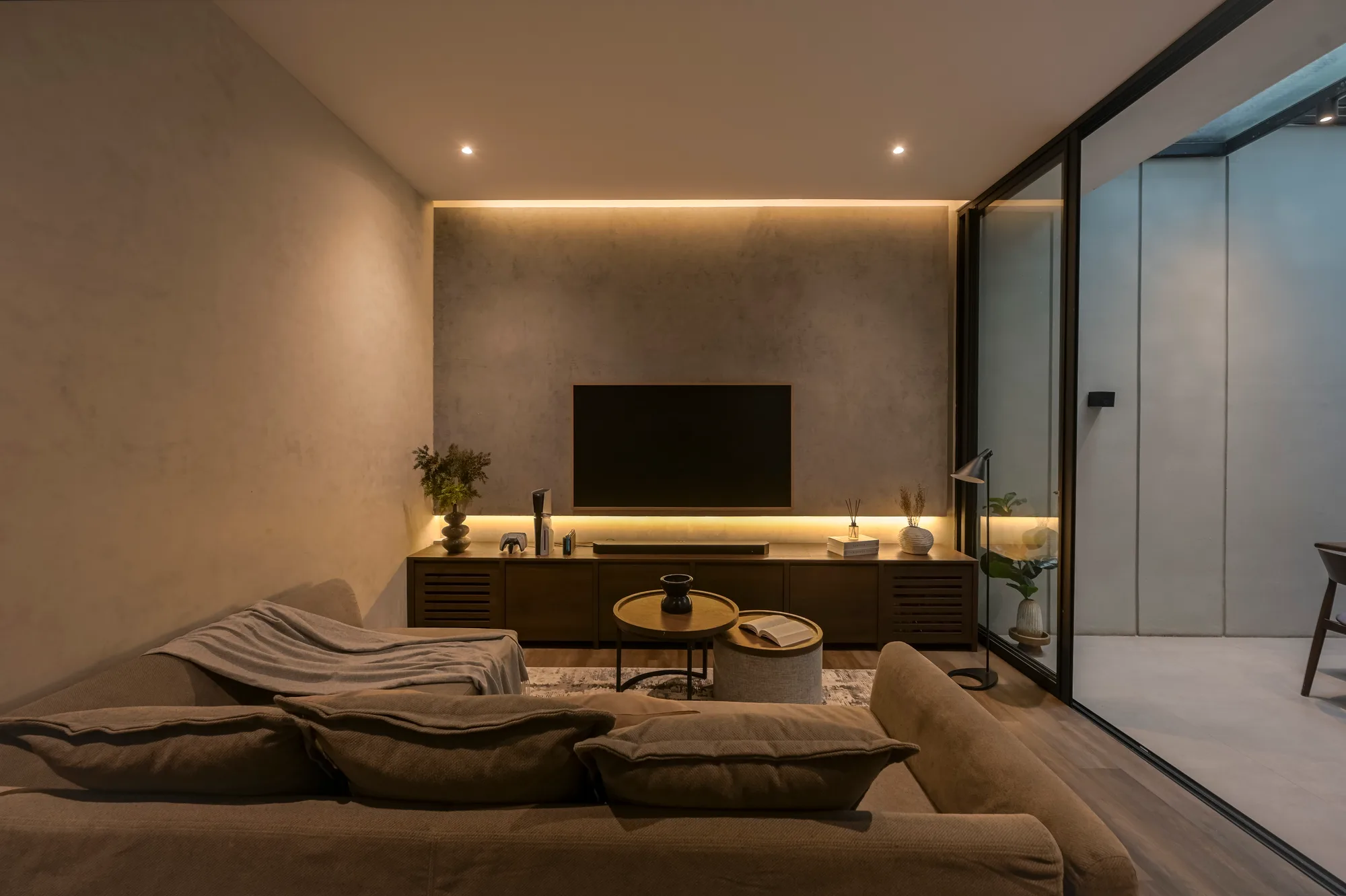 Living room sofa facing a concrete-look wall lit by a hidden cove above the wall-mounted television.