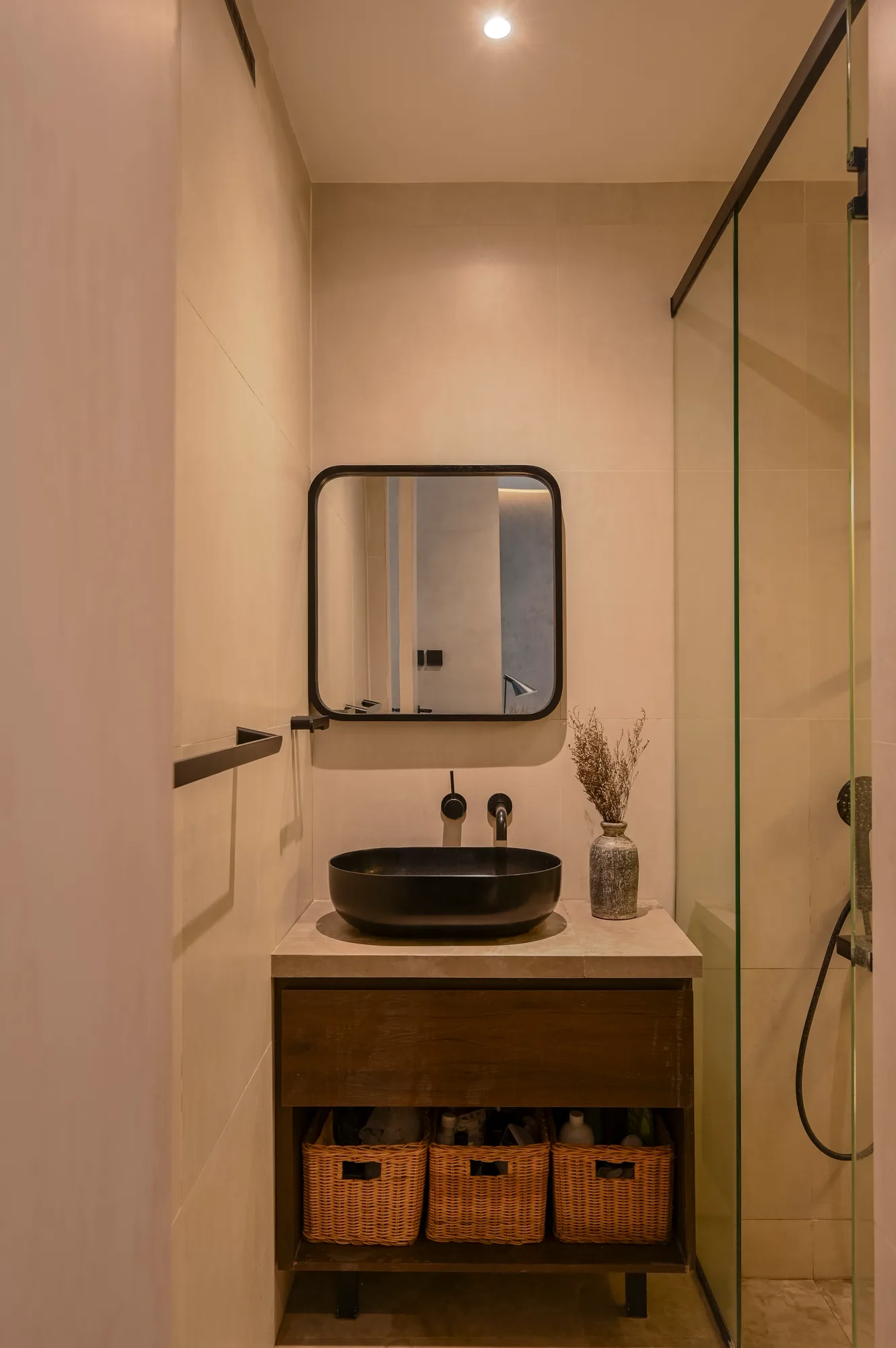 Powder room vanity with a black basin, square mirror, and woven baskets stored below.
