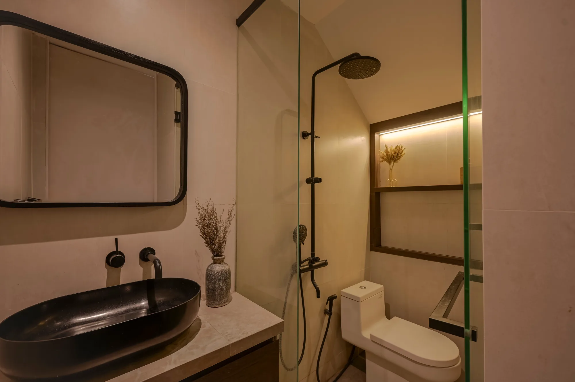 Bathroom shower fixture and toilet, black fittings against a recessed window shelf.
