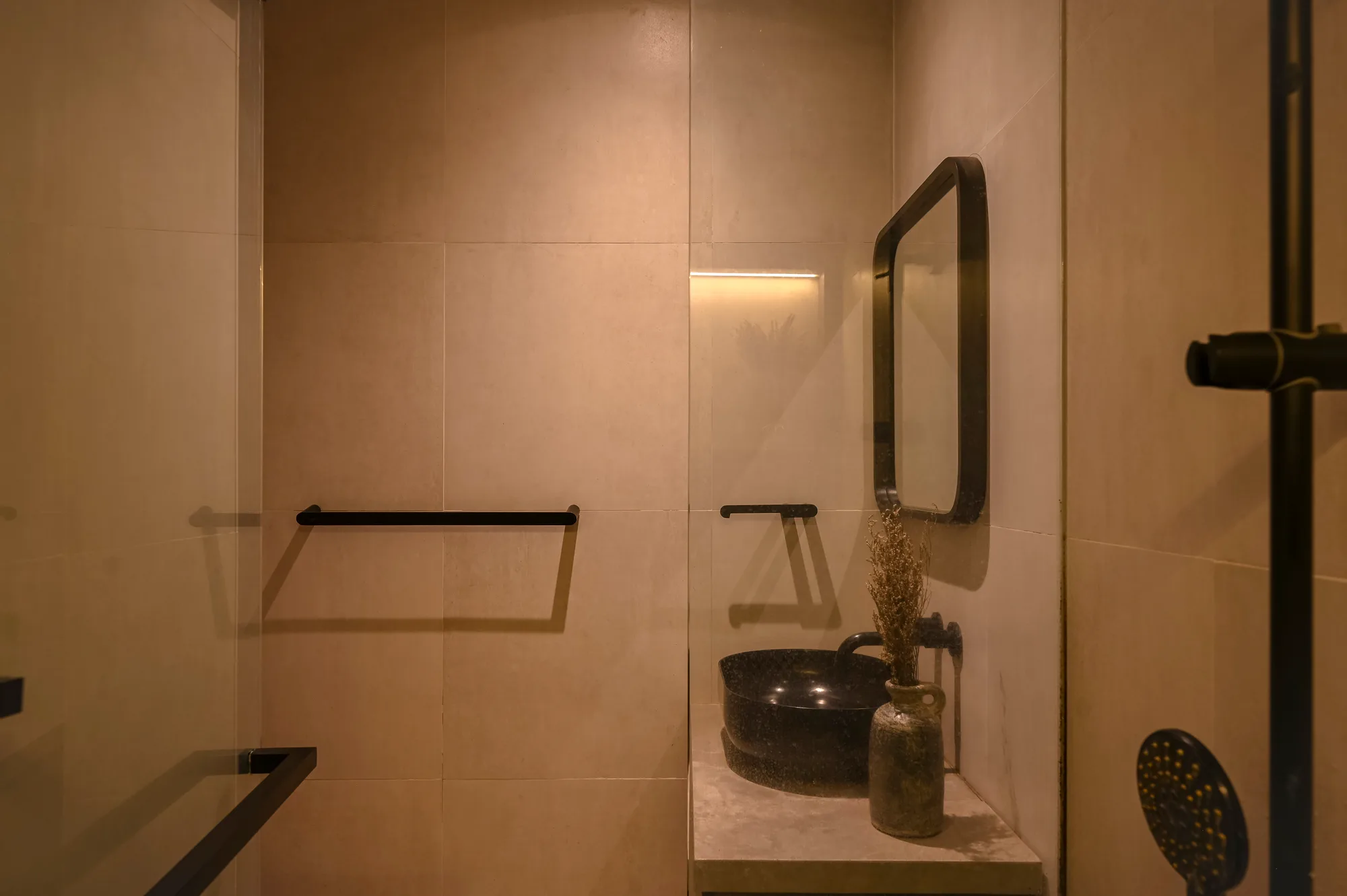 Bathroom vanity with an oval black basin, framed mirror, and shower fixture at the edge of frame.