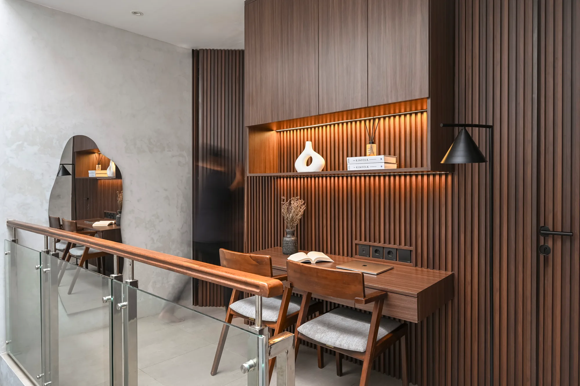 Upstairs landing with a slatted wood wall, display shelf, and desk nook behind a glass balustrade.