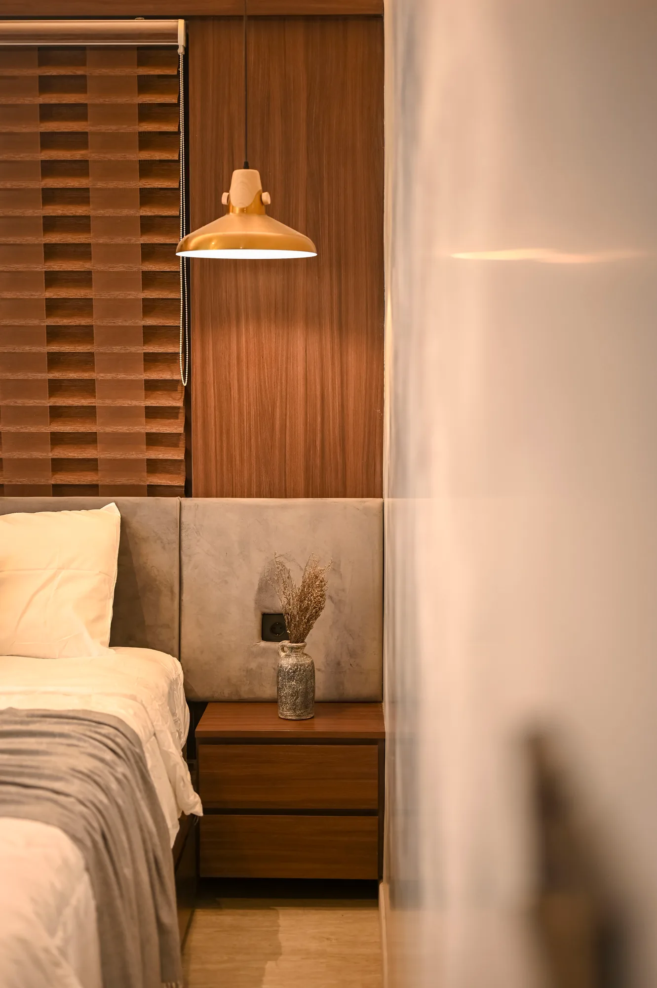 Brass pendant lamp hanging beside the woven wood headboard and bedside table.