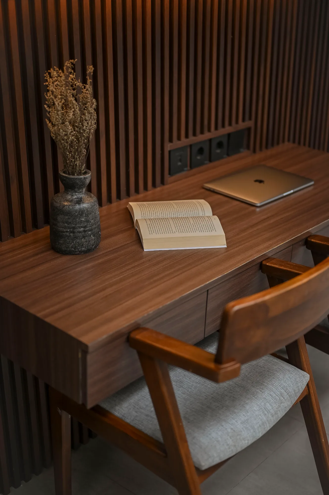 Desk detail with an open book and laptop against the slatted wood wall.