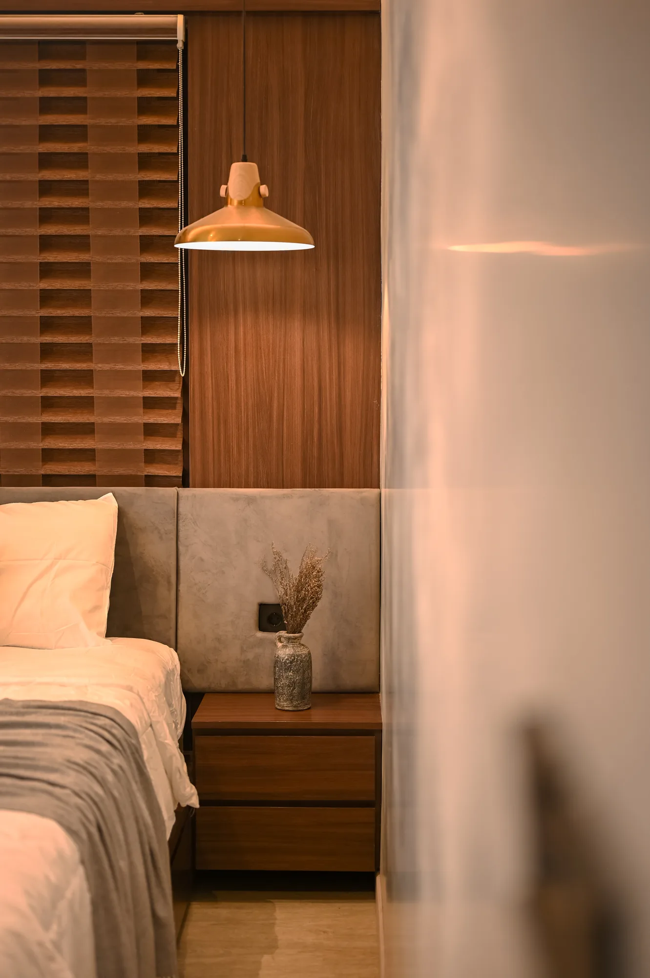 Brass pendant lamp and woven wood headboard panel beside the bed.