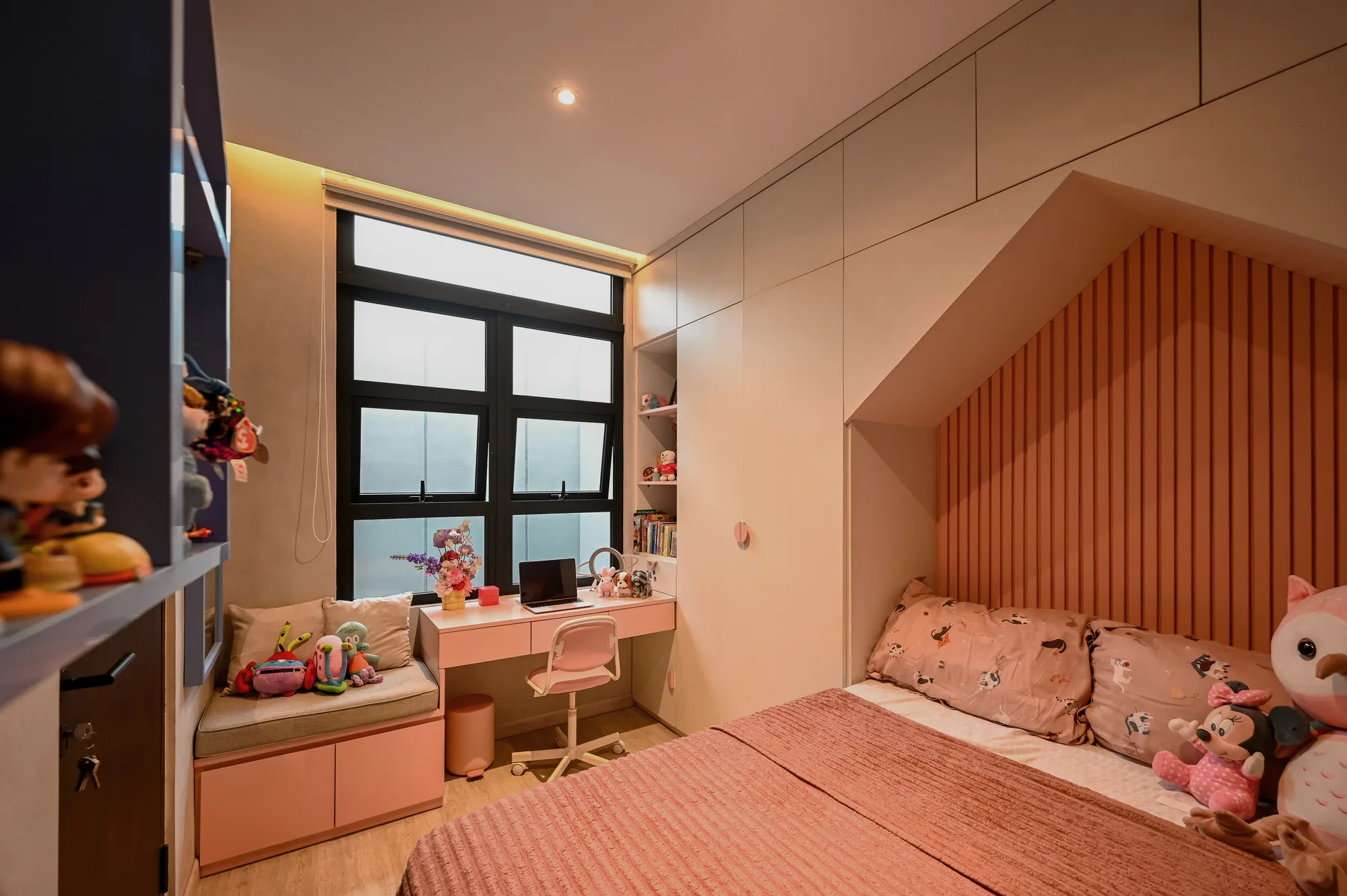 Children's bedroom with a built-in window seat, desk, and a slatted nook housing a single bed.