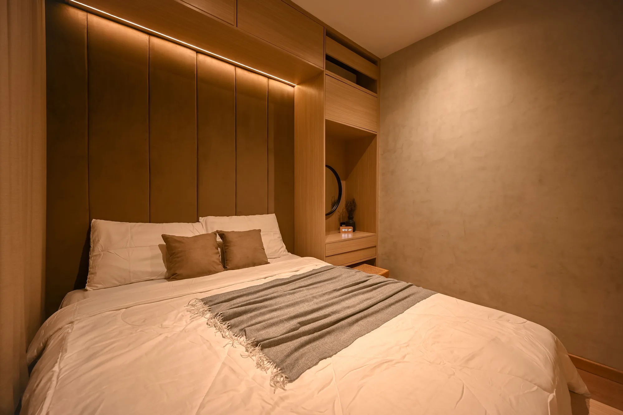 Bed with a channel-tufted headboard lit by a concealed light strip, the built-in vanity beside it.