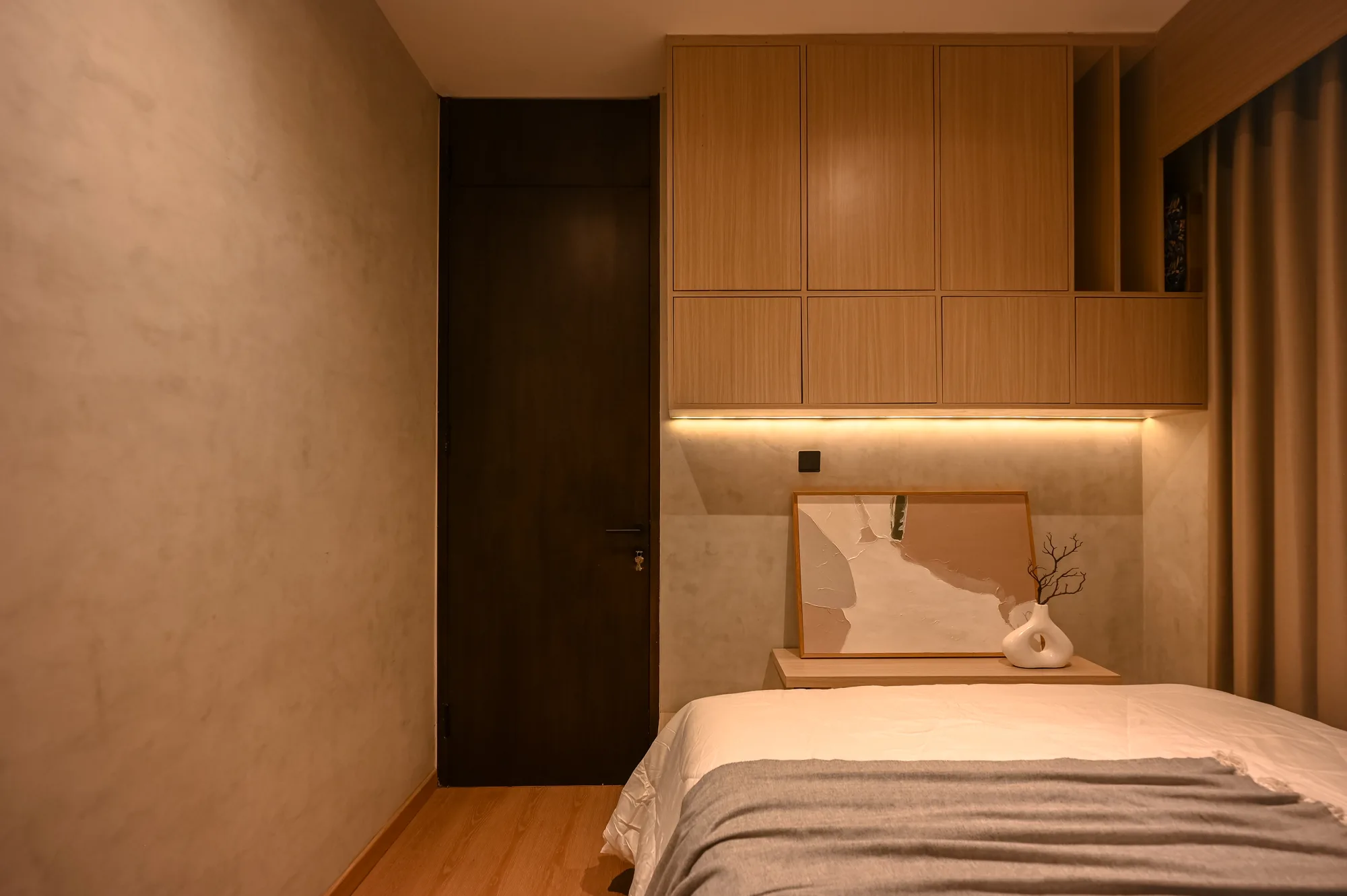 Bedroom nightstand with a framed abstract print and ceramic vase against the concrete-look wall.