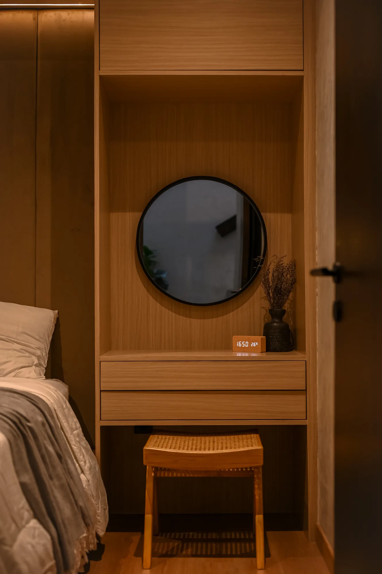 Round mirror and digital clock on the built-in vanity shelf beside a cane stool.