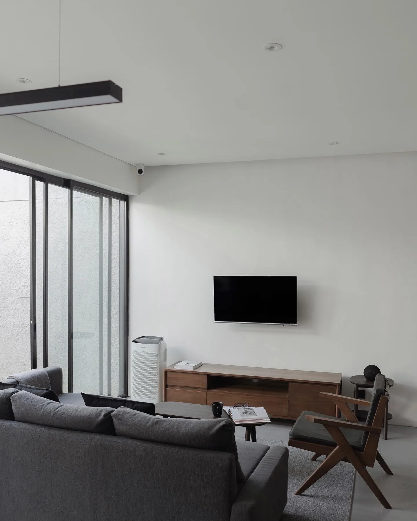 NM House's living room, a wall-mounted TV above a walnut credenza, grey sectional sofa and a wood-framed lounge chair.