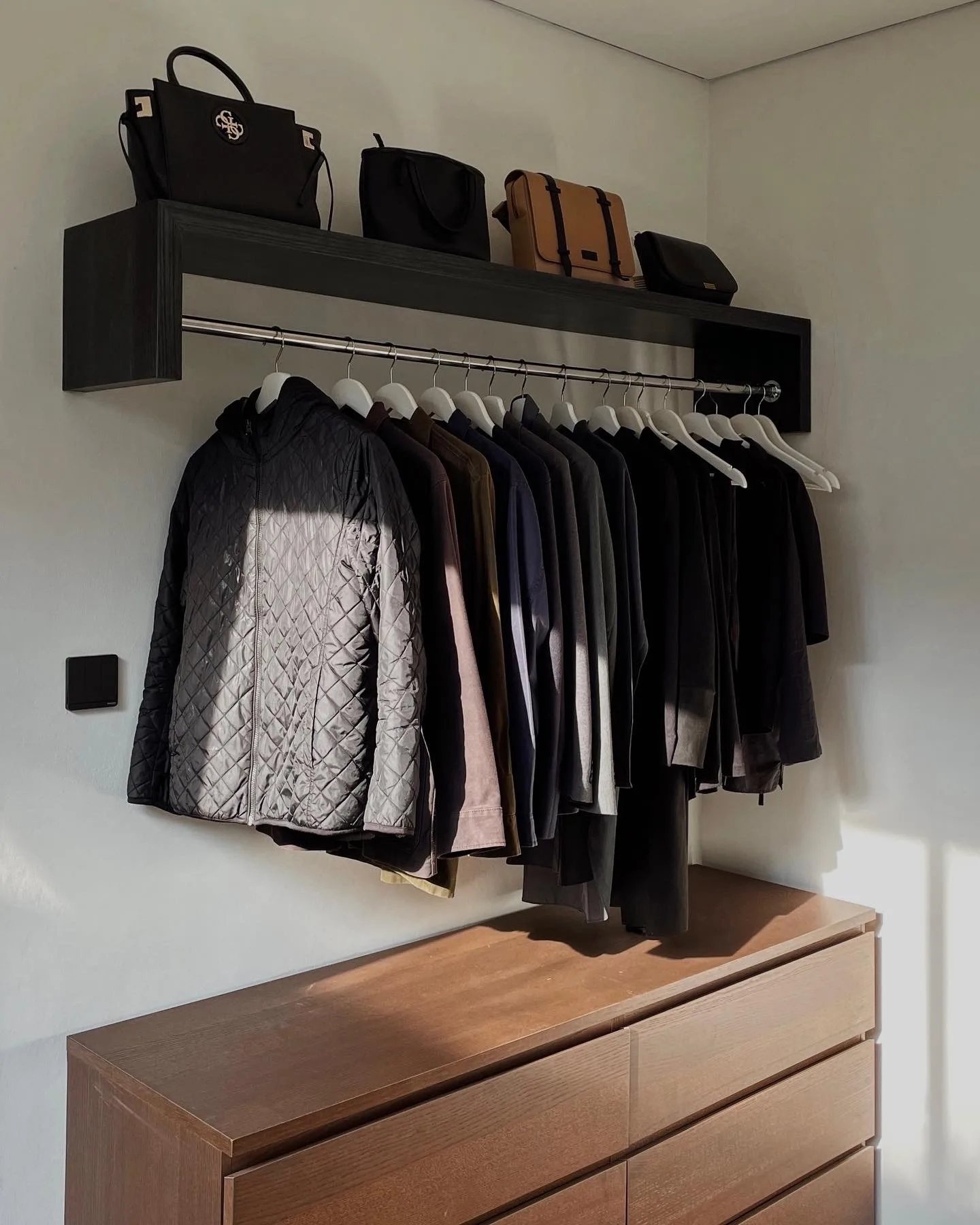 An open wardrobe rail, handbags lined on the shelf above hanging jackets and shirts.