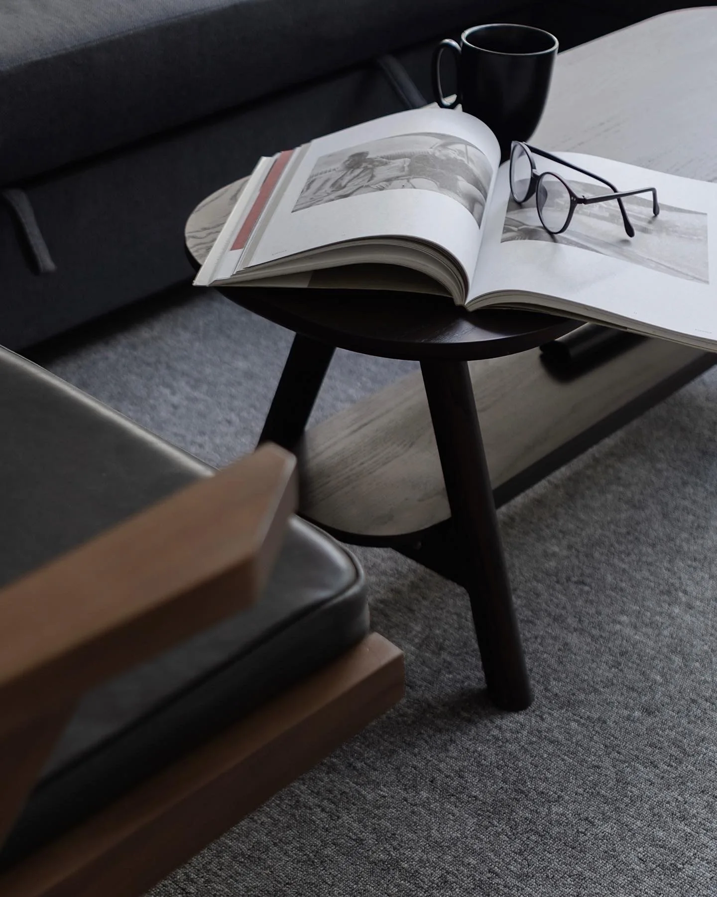 A round side table holding a black mug, an open photo book and a pair of glasses.