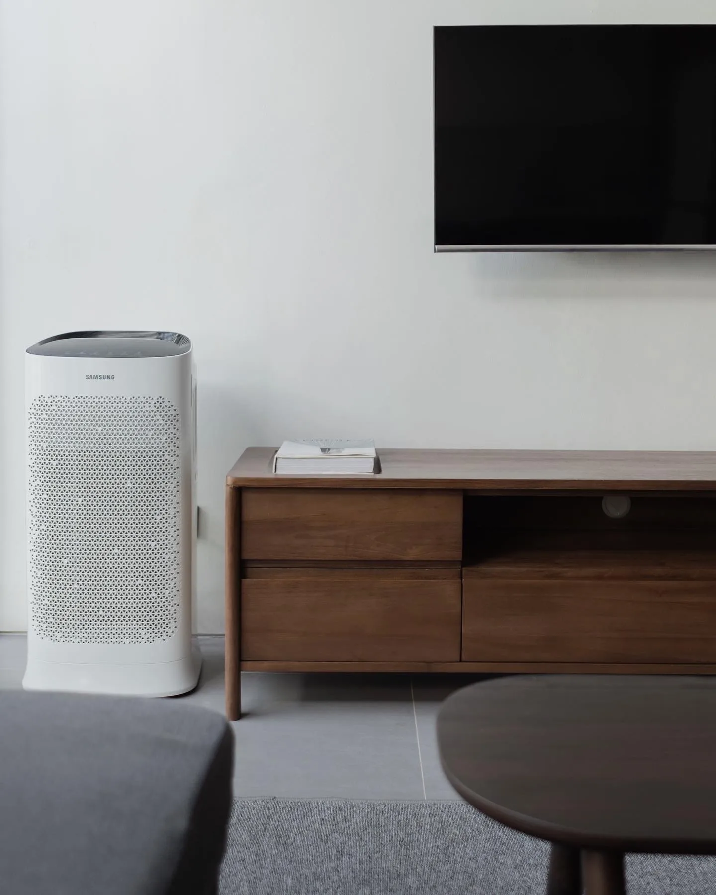 A wall-mounted TV above a walnut credenza, a white air purifier standing beside it.