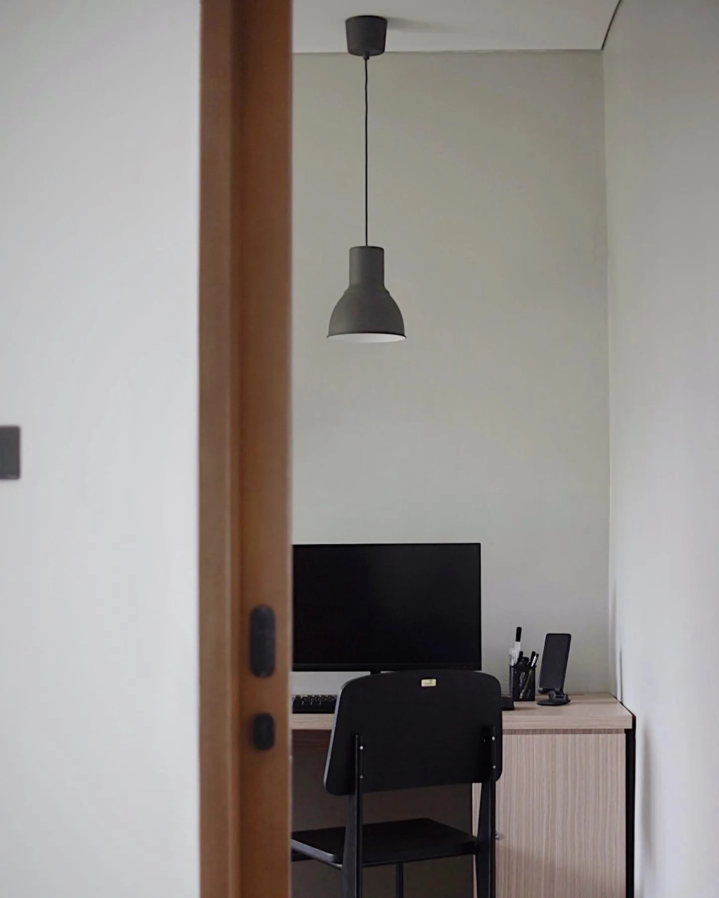 A doorway view into the home office, a pendant lamp over a desk with a monitor and keyboard.