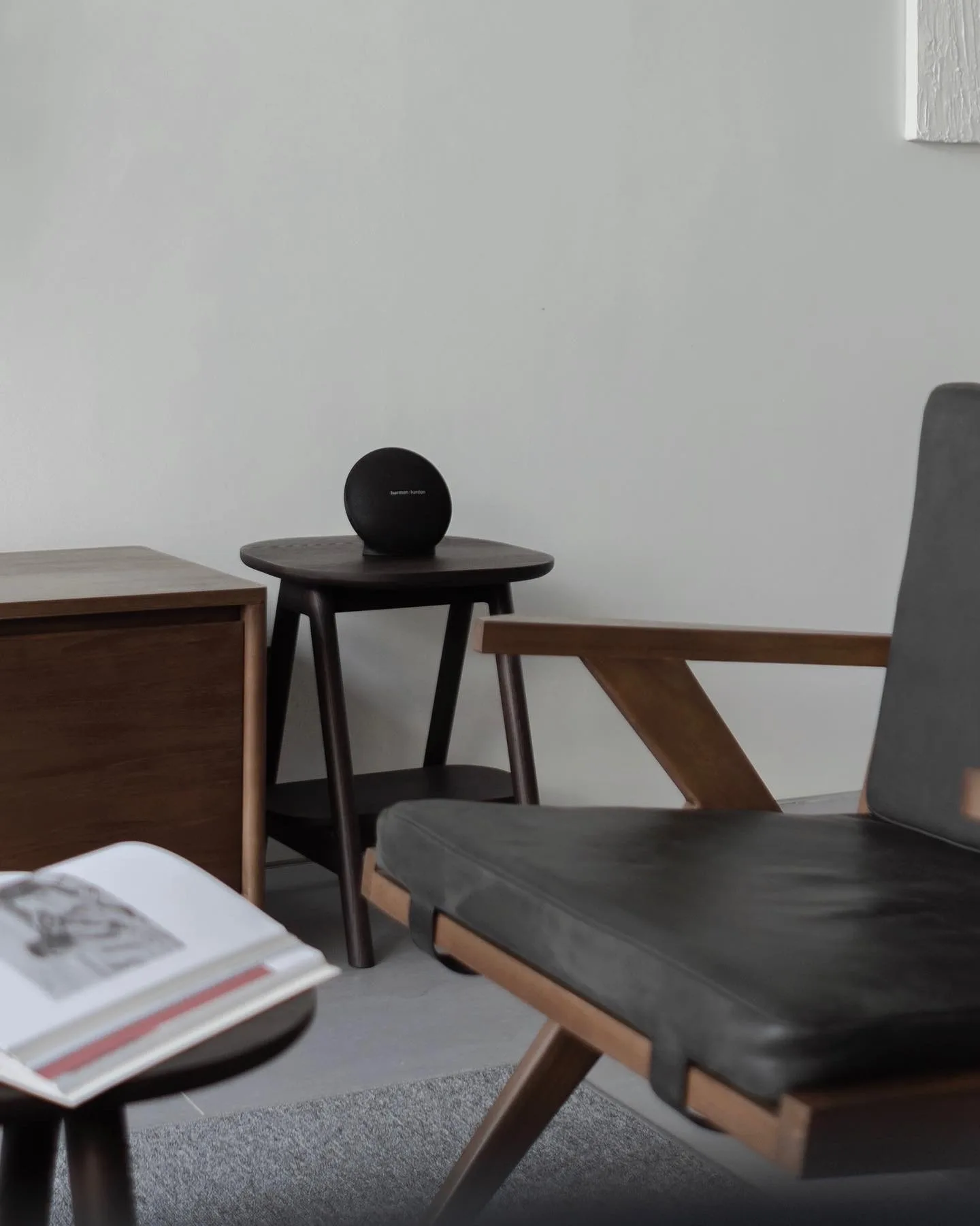 A round speaker on a dark wood side table beside a black leather lounge chair.
