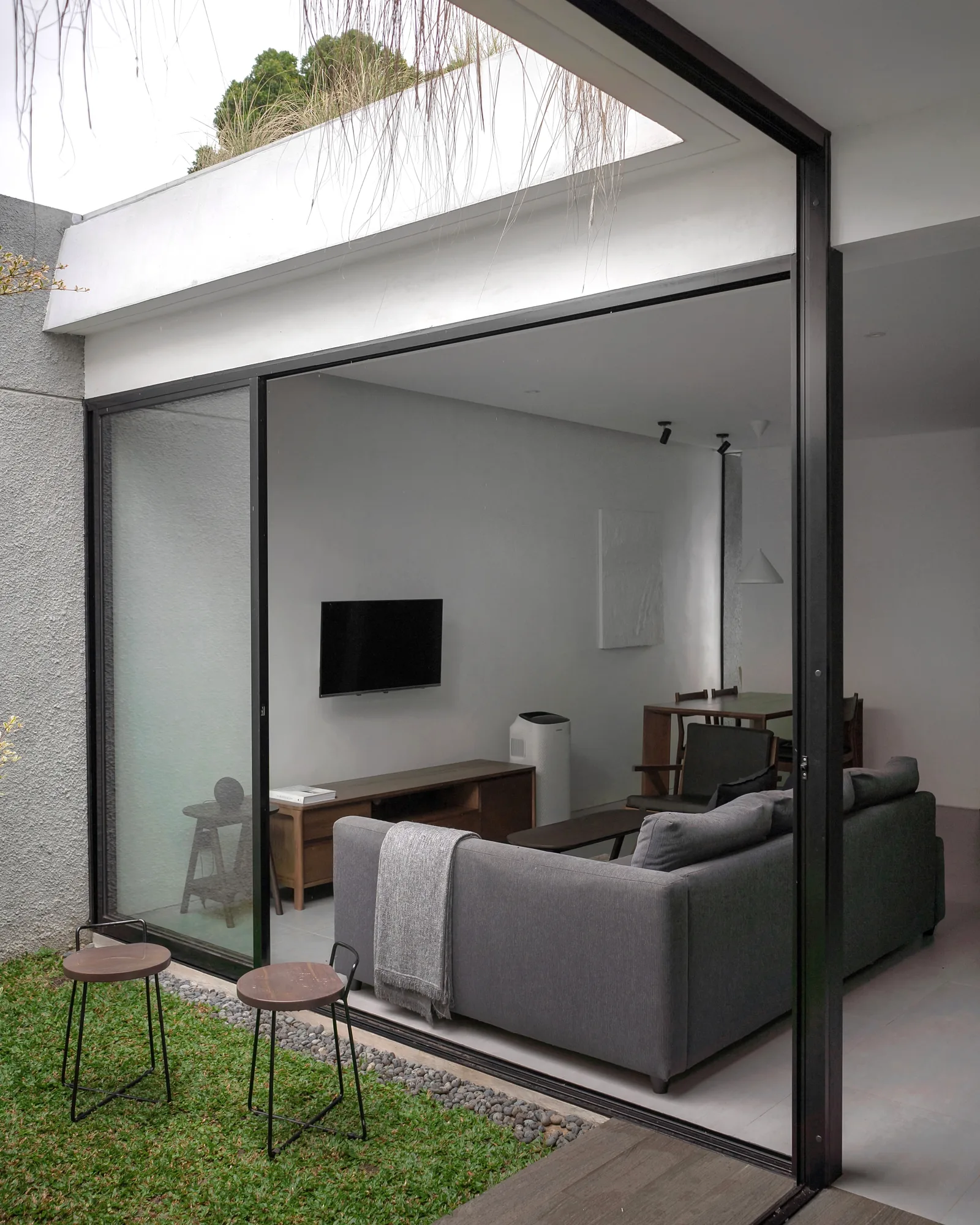 Rain on the glass sliding door beside the inner court's tree, the darkened living room visible through it.