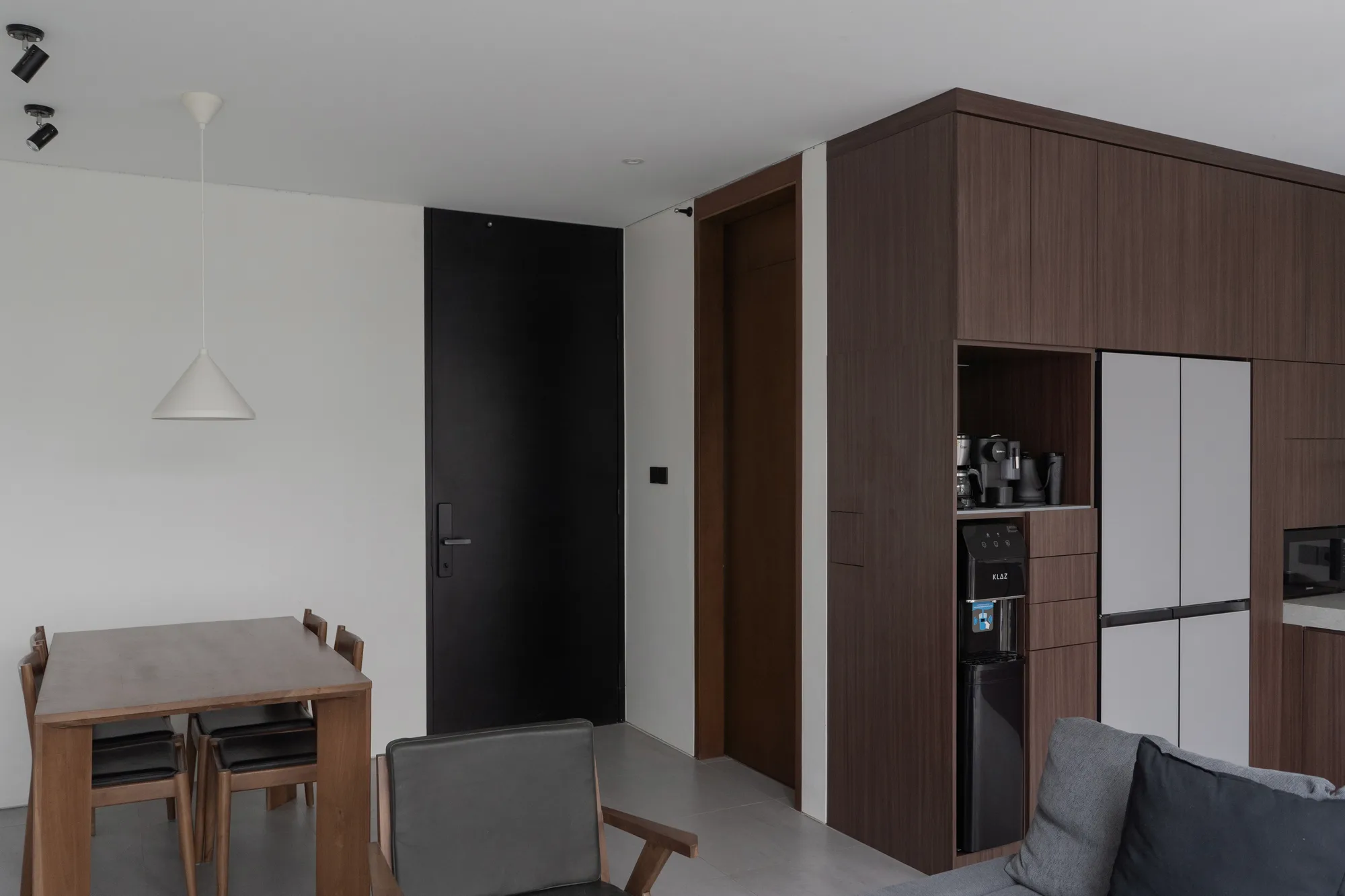 A wide view through the glass partition: the living area on one side, the dining table and kitchen coffee station on the other.