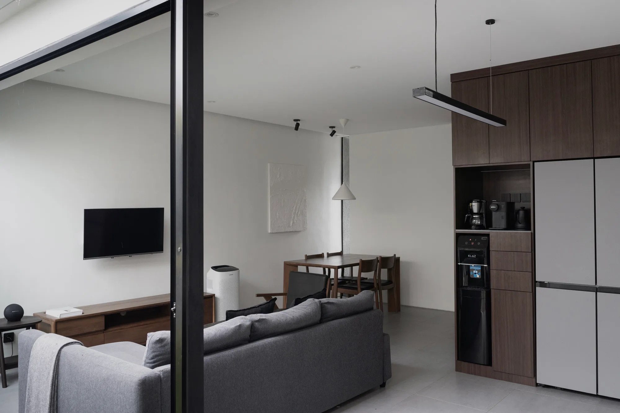 A diagonal view through the glass partition toward the dining table and kitchen, the living room in the foreground.