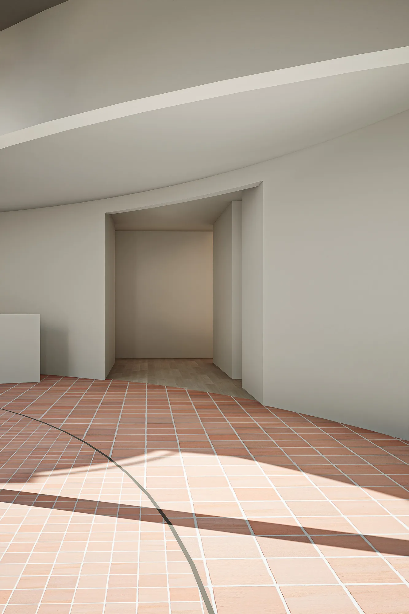 Curved white passage opening onto a recessed doorway, the terracotta courtyard floor sweeping past in daylight.