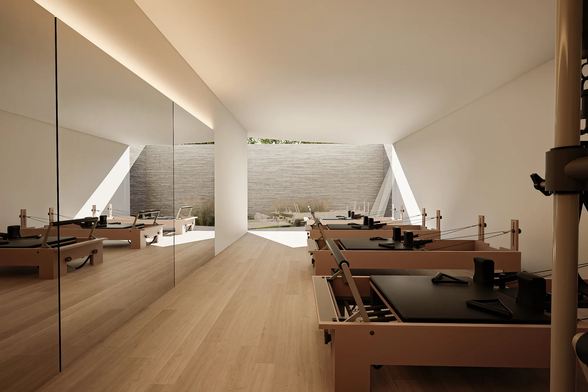 Pilates studio with reformer machines on oak flooring, mirror wall reflecting the ribbed exterior wall beyond the glass.