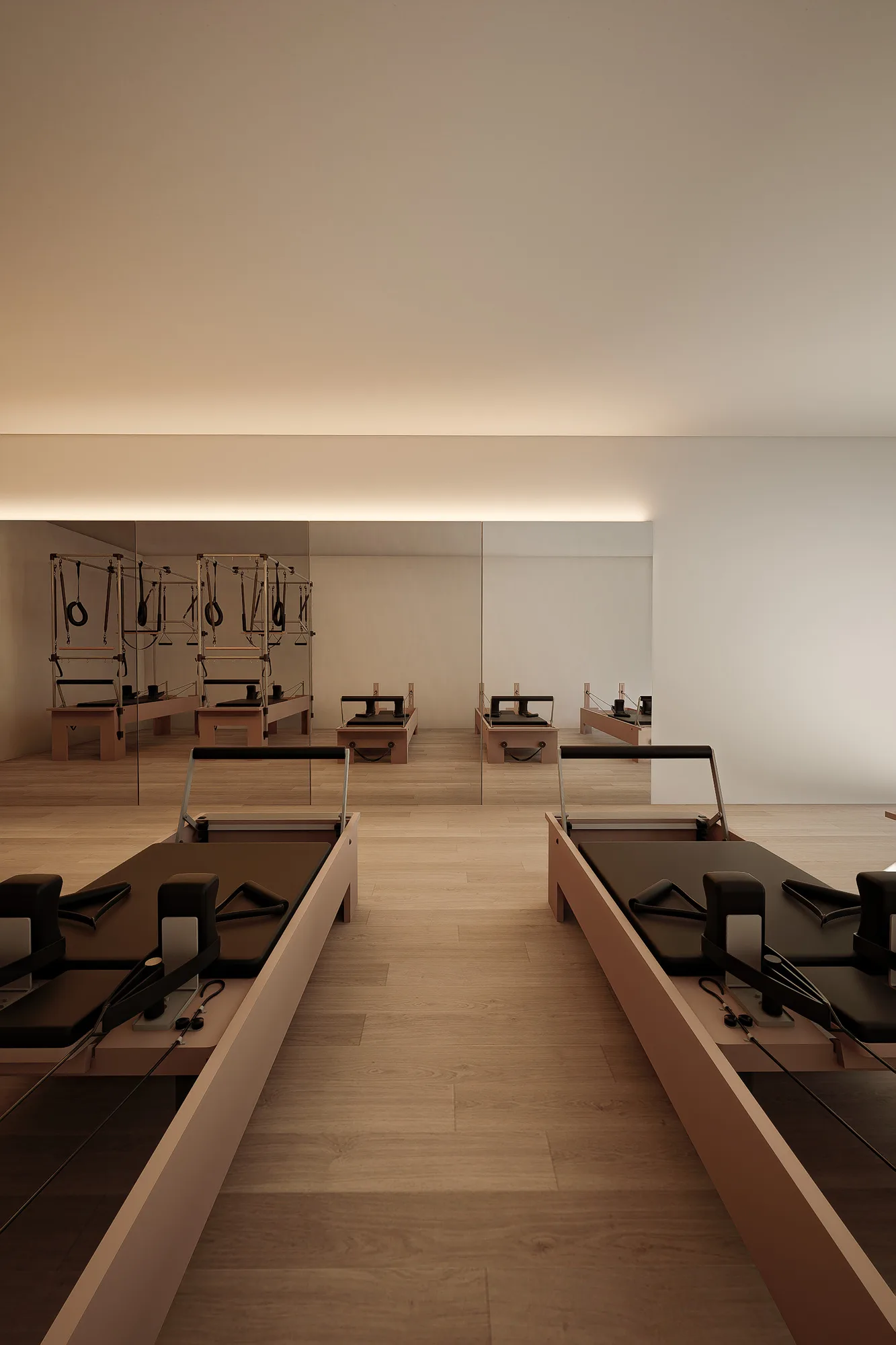 Pilates reformers facing a full-height mirror wall that doubles the equipment and oak flooring in reflection.