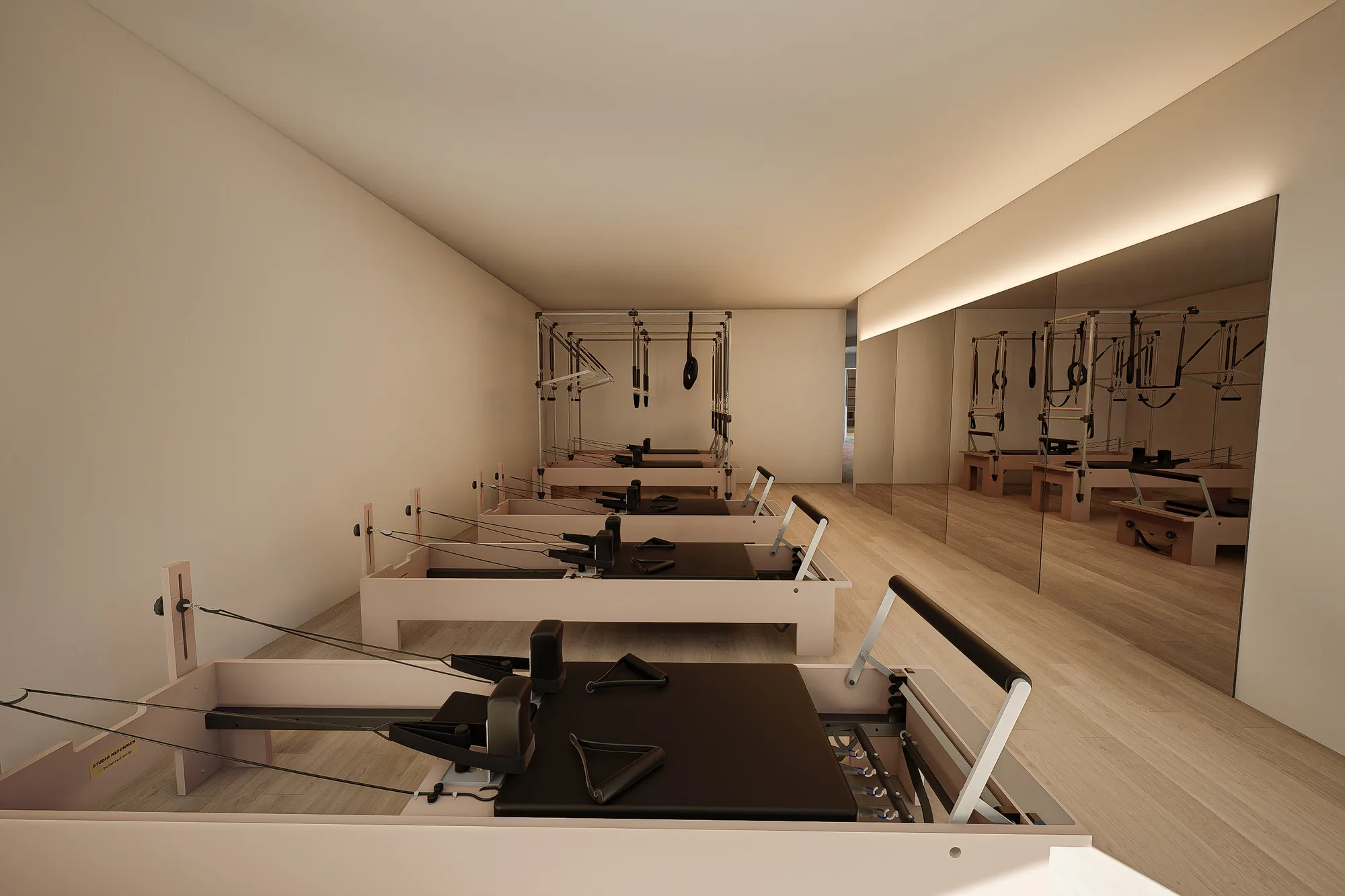Row of reformers and a hanging trapeze frame arranged along the pilates studio's mirror wall.