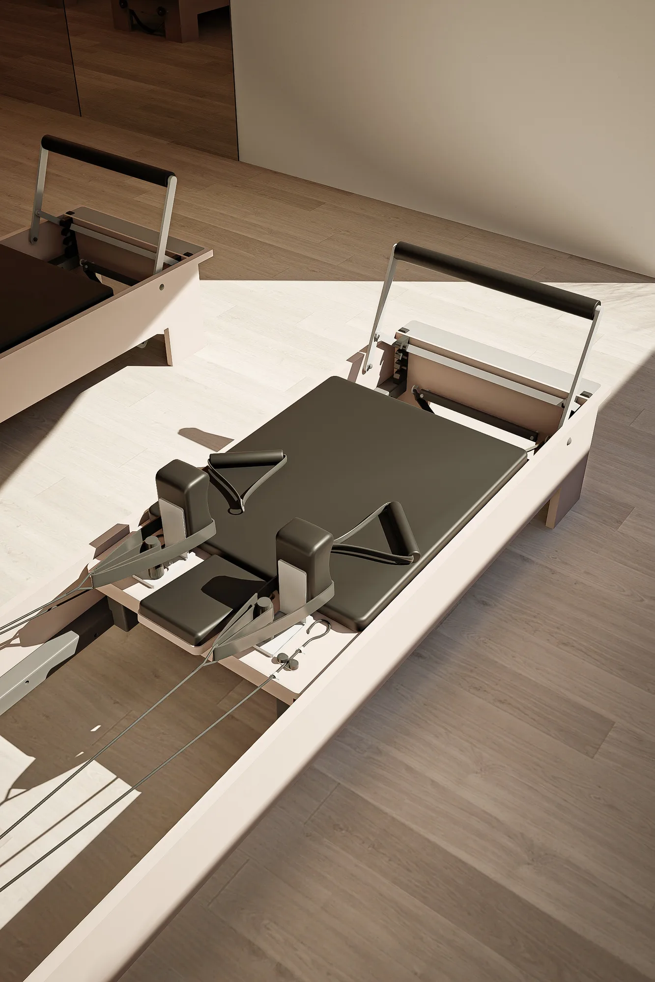 Overhead detail of a pilates reformer's straps and carriage on the studio's light oak flooring.