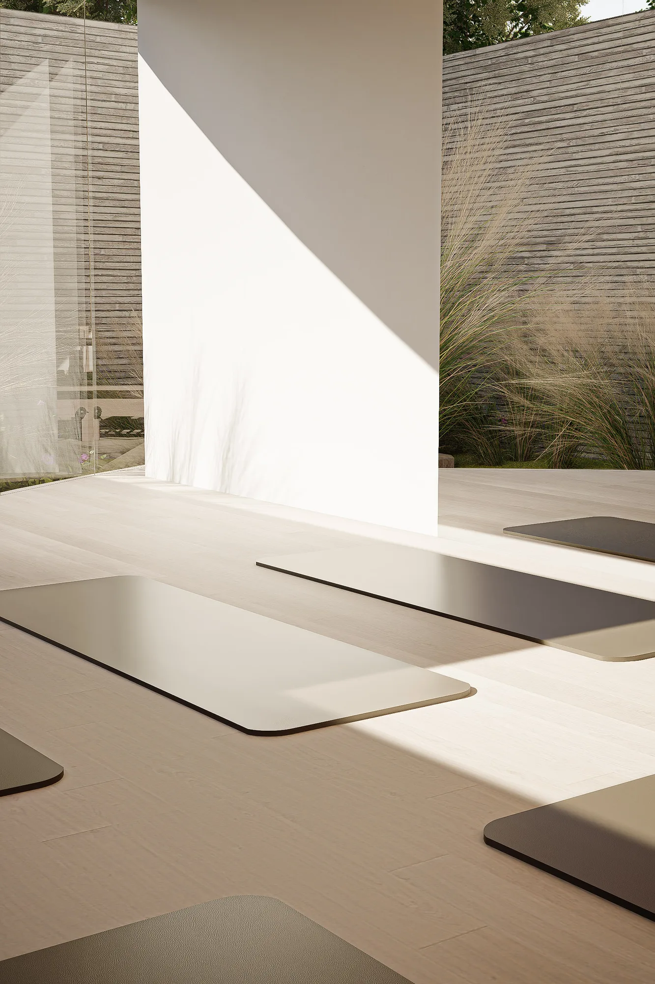 Exercise mats laid on oak flooring beside a sunlit courtyard wall with tall grass planted along the board-formed perimeter.