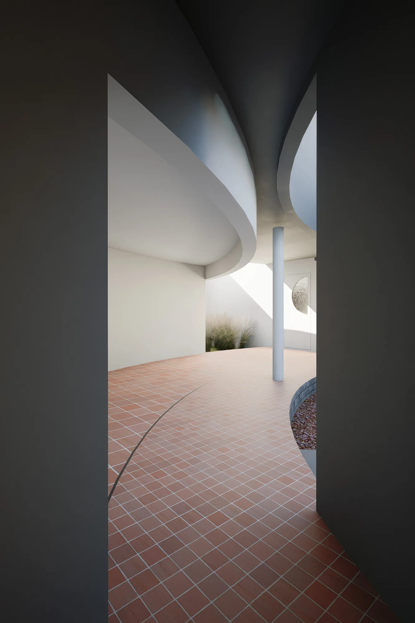 Covered walkway between two curved board-formed walls opening onto a planted courtyard edge.
