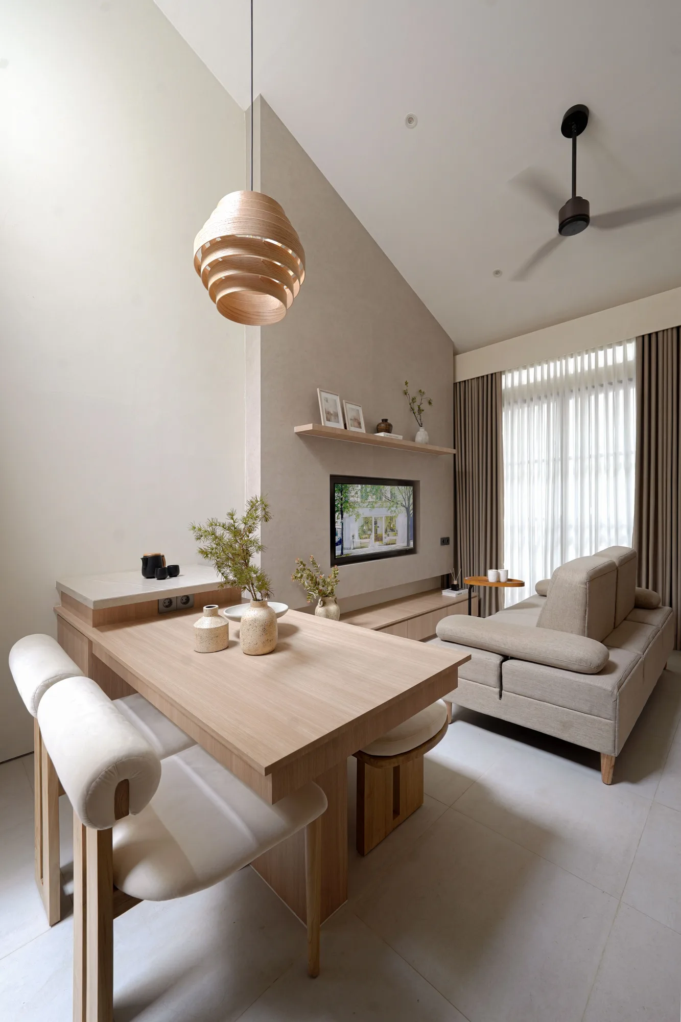 Double-height living room with a pale timber dining table, linen sofa and sculptural timber pendant light.