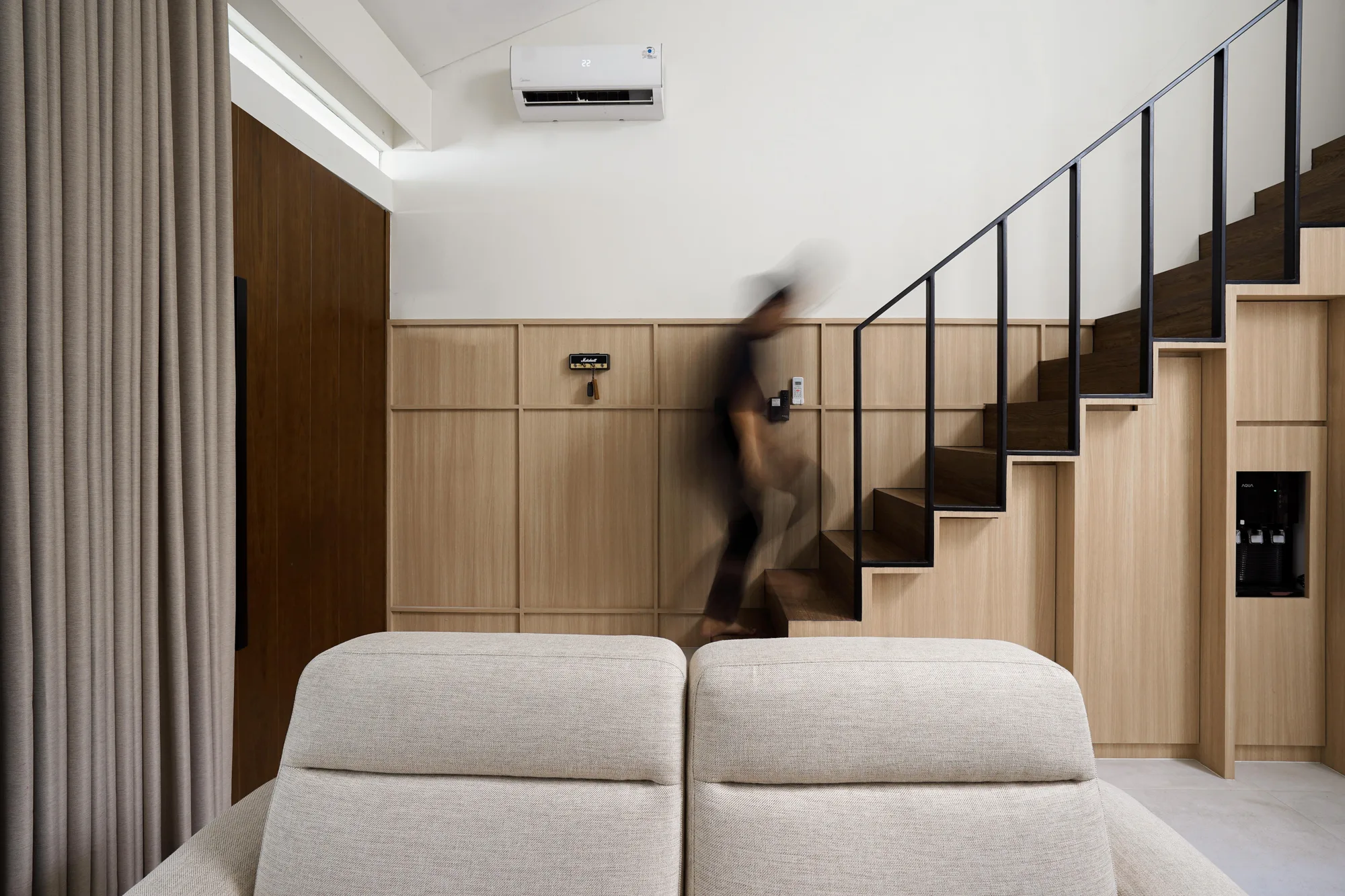 Living room seating facing a dark-tread stair, its black steel railing integrated with pale timber joinery.