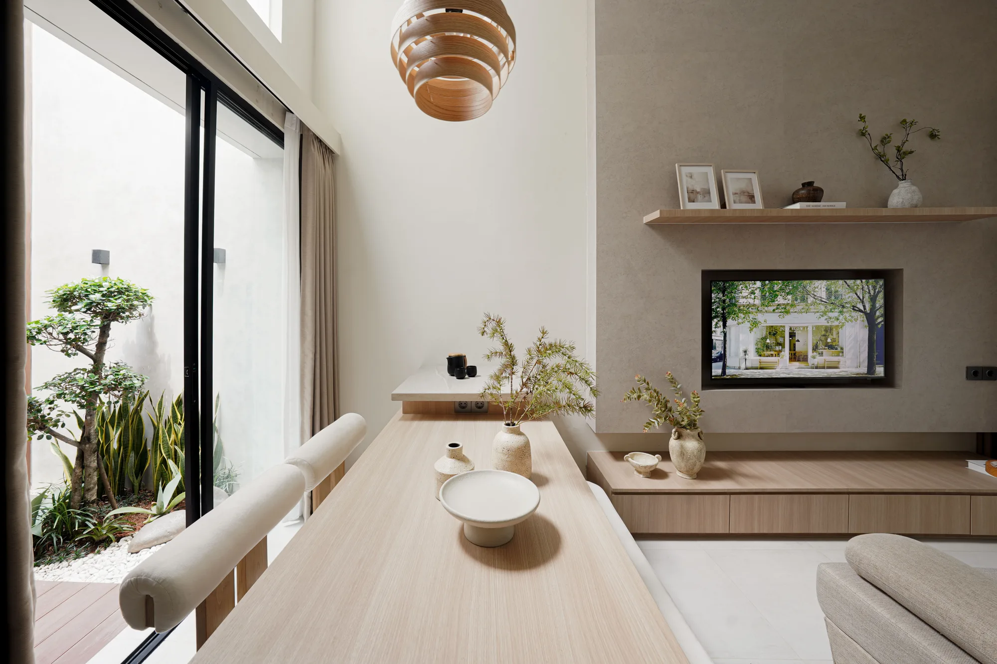 Dining table beside the courtyard, facing a recessed television wall with a floating timber shelf.